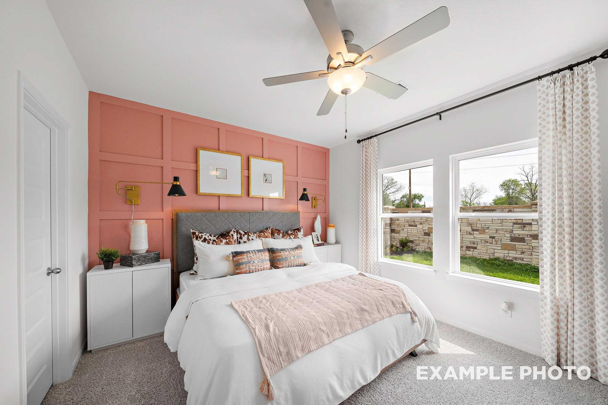 Cozy bedroom with pink panel accent wall and ceiling fan in The Sabine E floor plan at Liberty Estates, Cleveland, Texas.