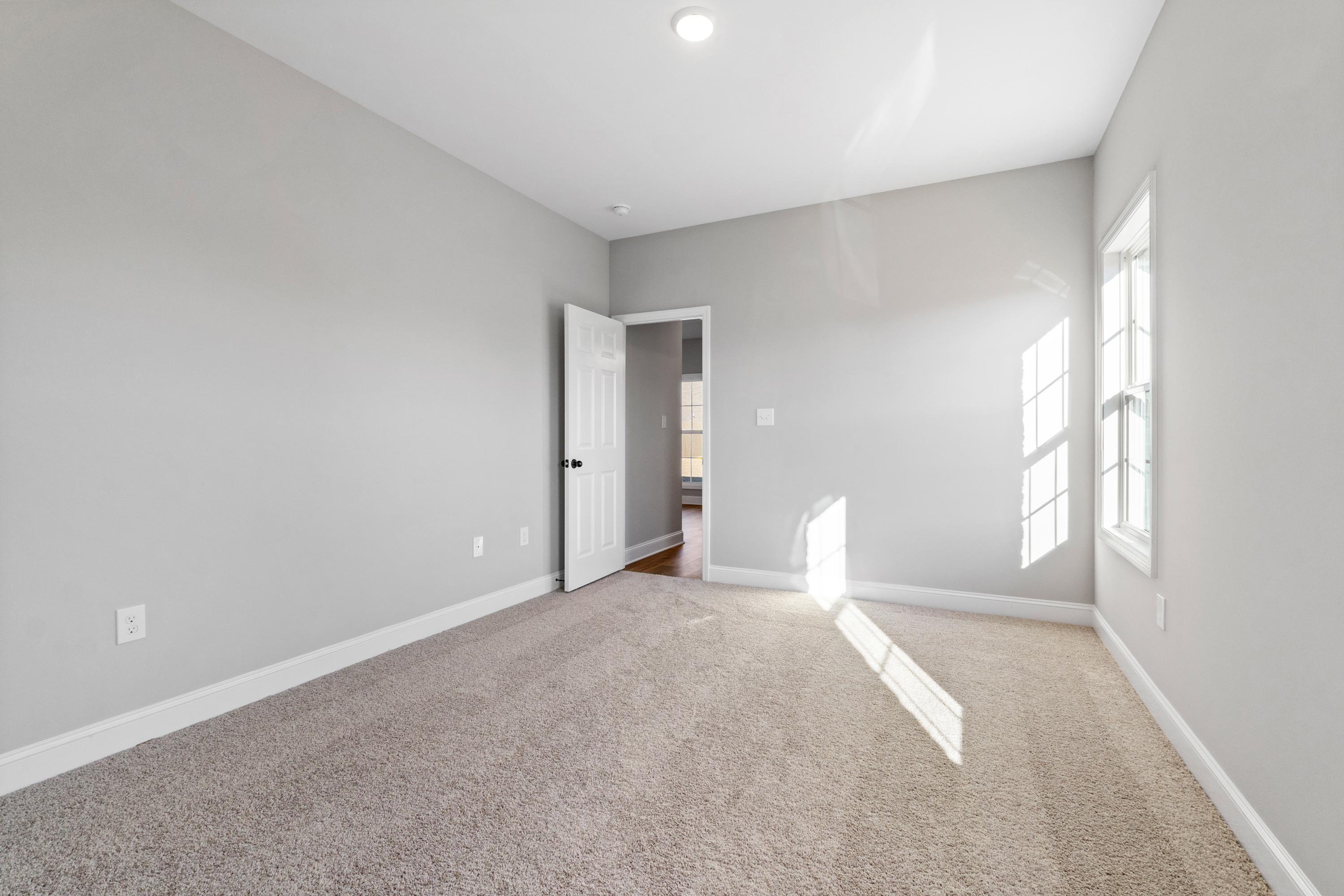Spacious bedroom in The Valencia home with gray walls, beige carpet, open door, and sunlight through windows