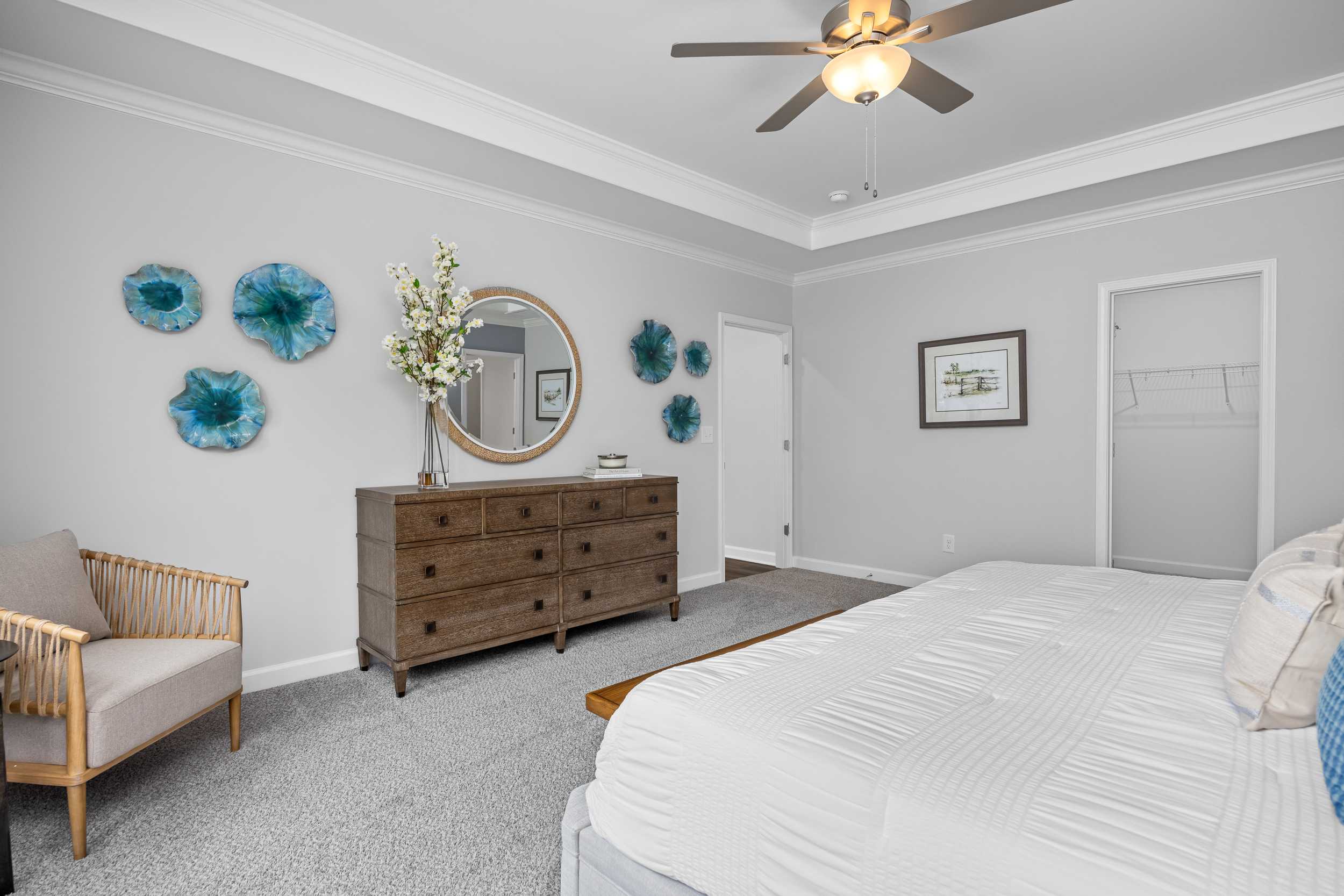 Spacious primary bedroom at Tobacco Road in Angier NC with gray walls, wooden dresser, ceiling fan and blue wall decor