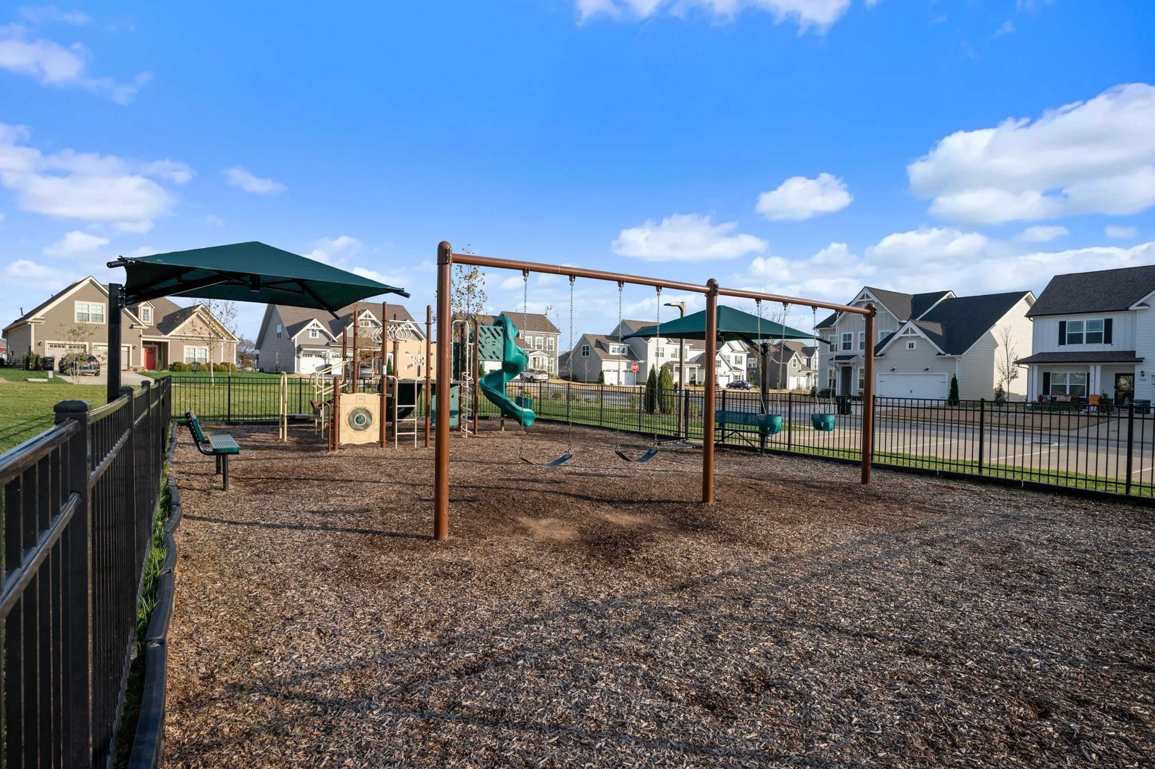 Children's playground at Shelton Square in Murfreesboro TN with swings, green slide, benches and fenced mulch area