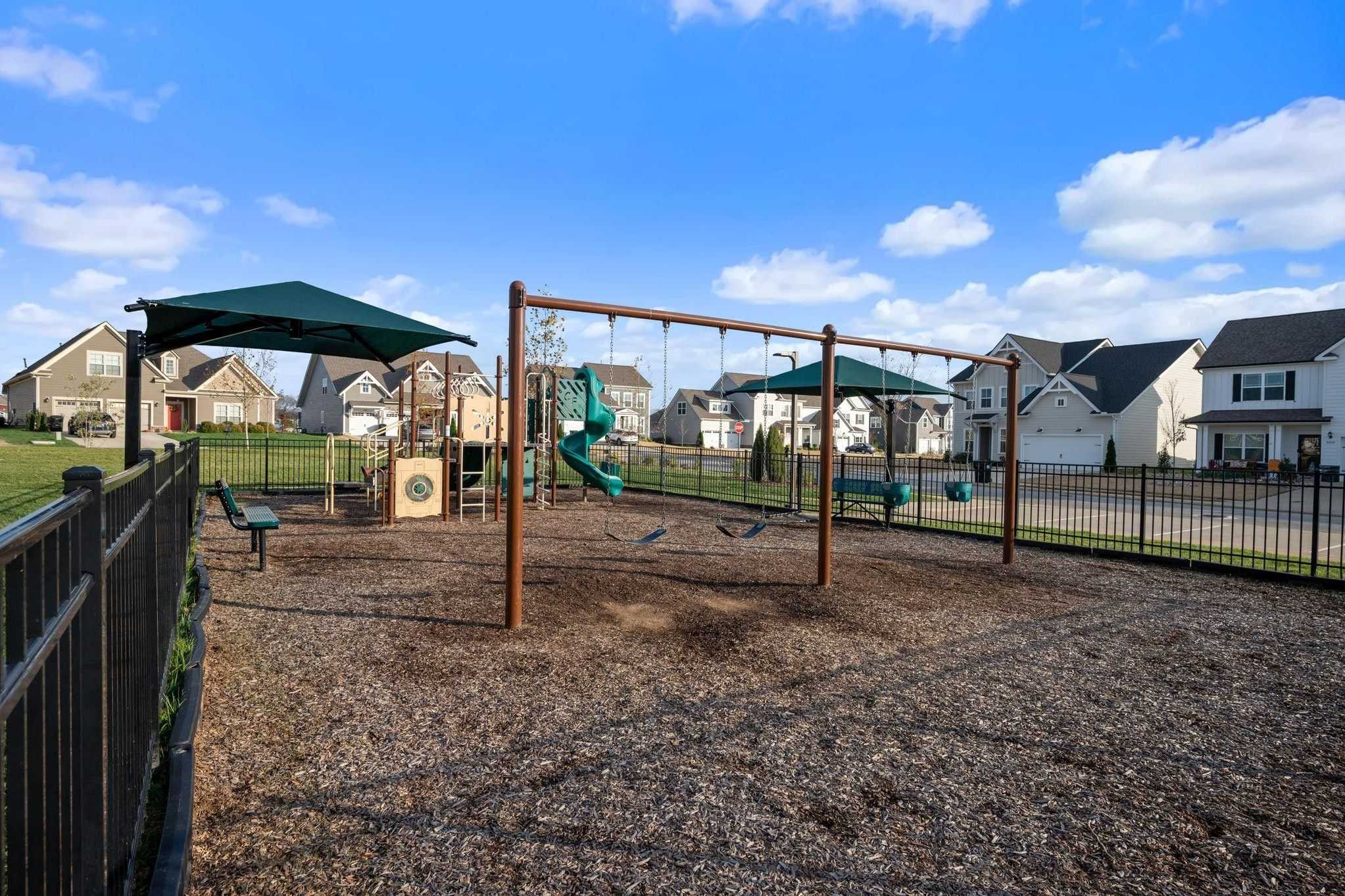 Children's playground at Shelton Square in Murfreesboro TN with swings, green slide, benches and fenced mulch area