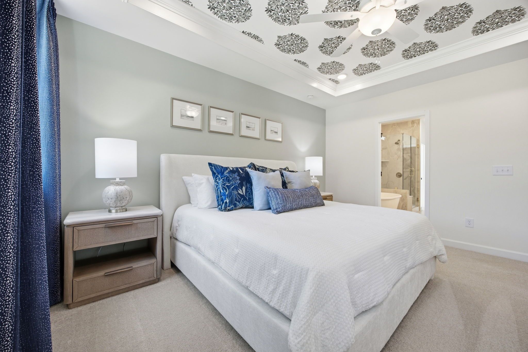Master suite of The Ashport featuring a tray ceiling with floral wallpaper and an attached bathroom in Wendell, NC.