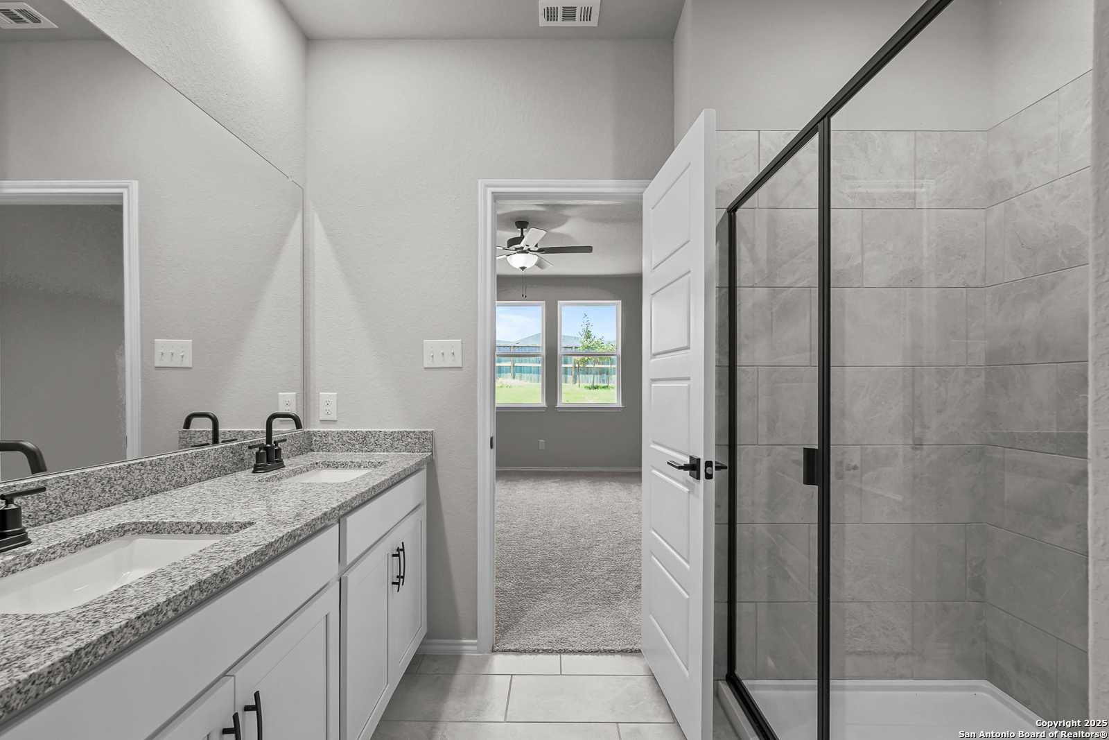 Modern master bathroom with double granite vanity, frameless glass shower, and bedroom view in Davidson Homes The Daphne K, San Antonio