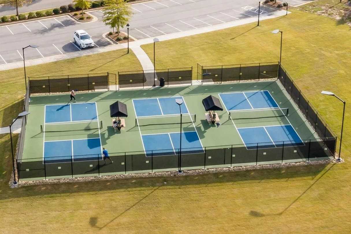 Four lighted tennis courts at Addison West in Holly Springs NC with blue surfaces, shaded pavilions, black fencing, and players