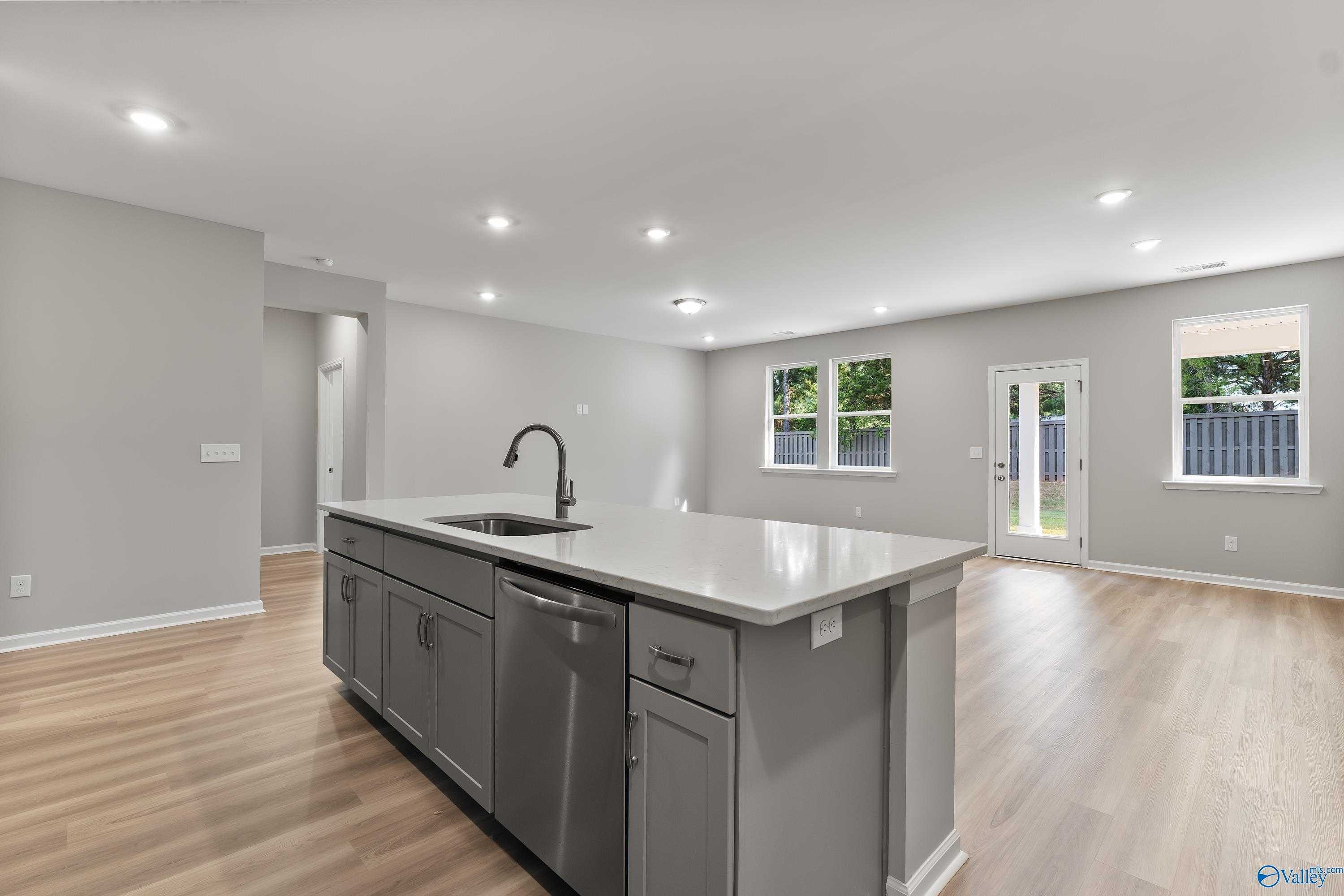 Modern kitchen island with white quartz countertop, gray cabinets, sink, and dishwasher in open-concept space, The Grace by Evermore Homes, Madison AL