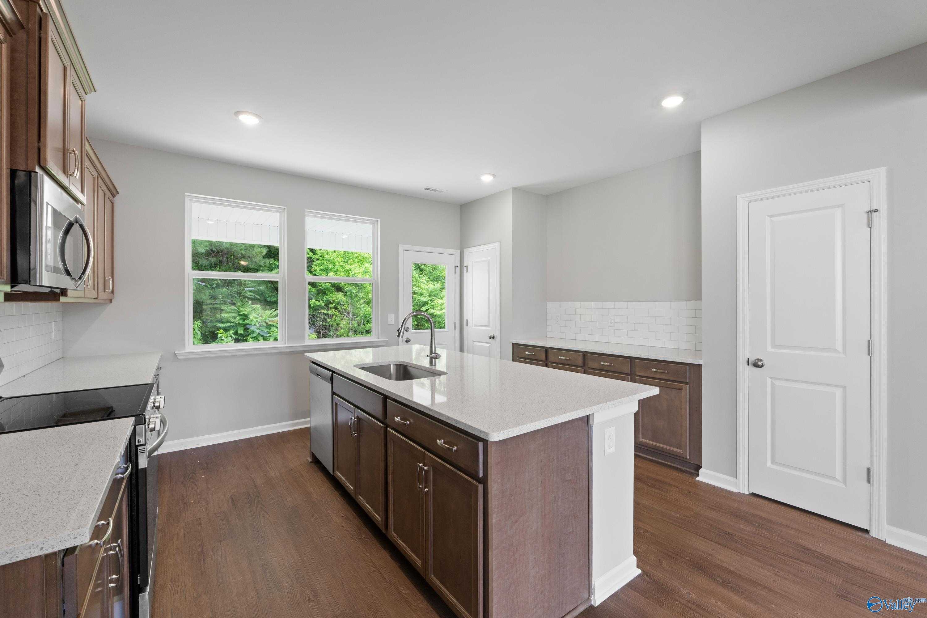Bright kitchen with white cabinets, quartz island, stainless appliances, and window views in Davidson Homes The Stella, Hazel Green, AL