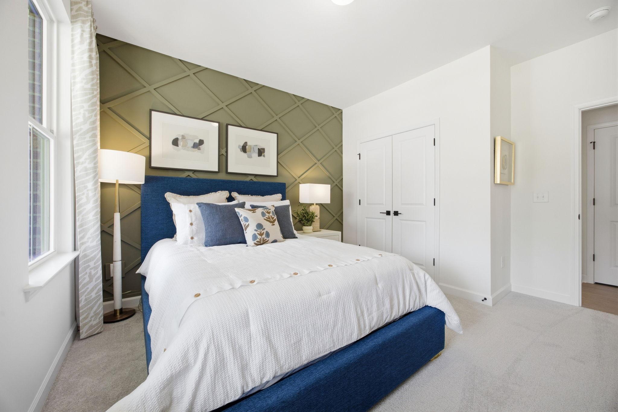 Cozy bedroom in The Ashport featuring a blue upholstered bed, green accent wall with wainscoting, and modern decor.