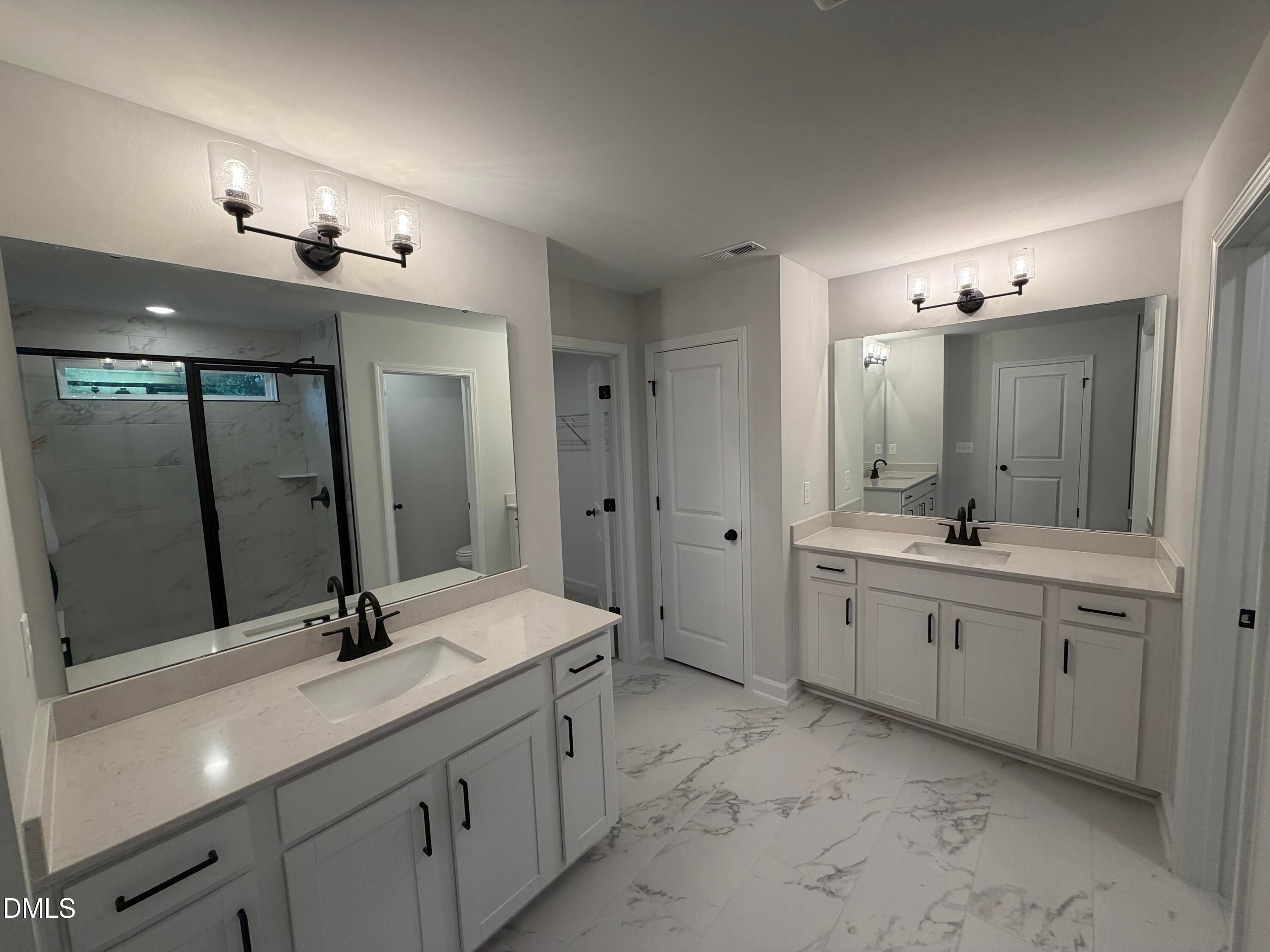 Double vanity primary bathroom with white cabinetry, marble tile shower, and black fixtures in The Preston C home, Wendell, NC
