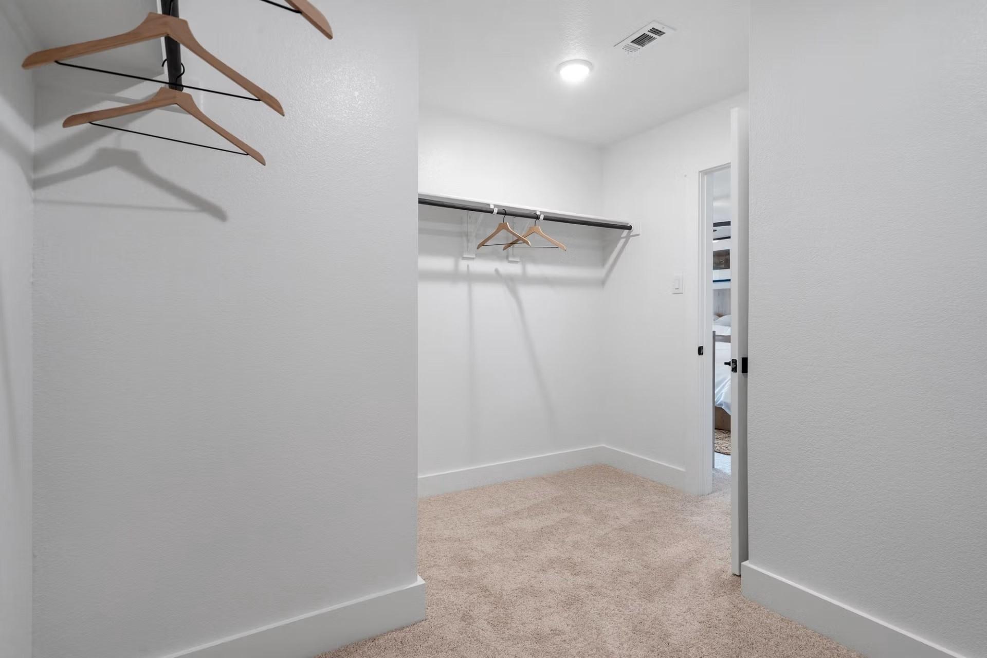 Spacious walk-in closet with wooden hangers, beige carpet, and open door in master suite, Davidson Homes The Wake D, Wylie Texas