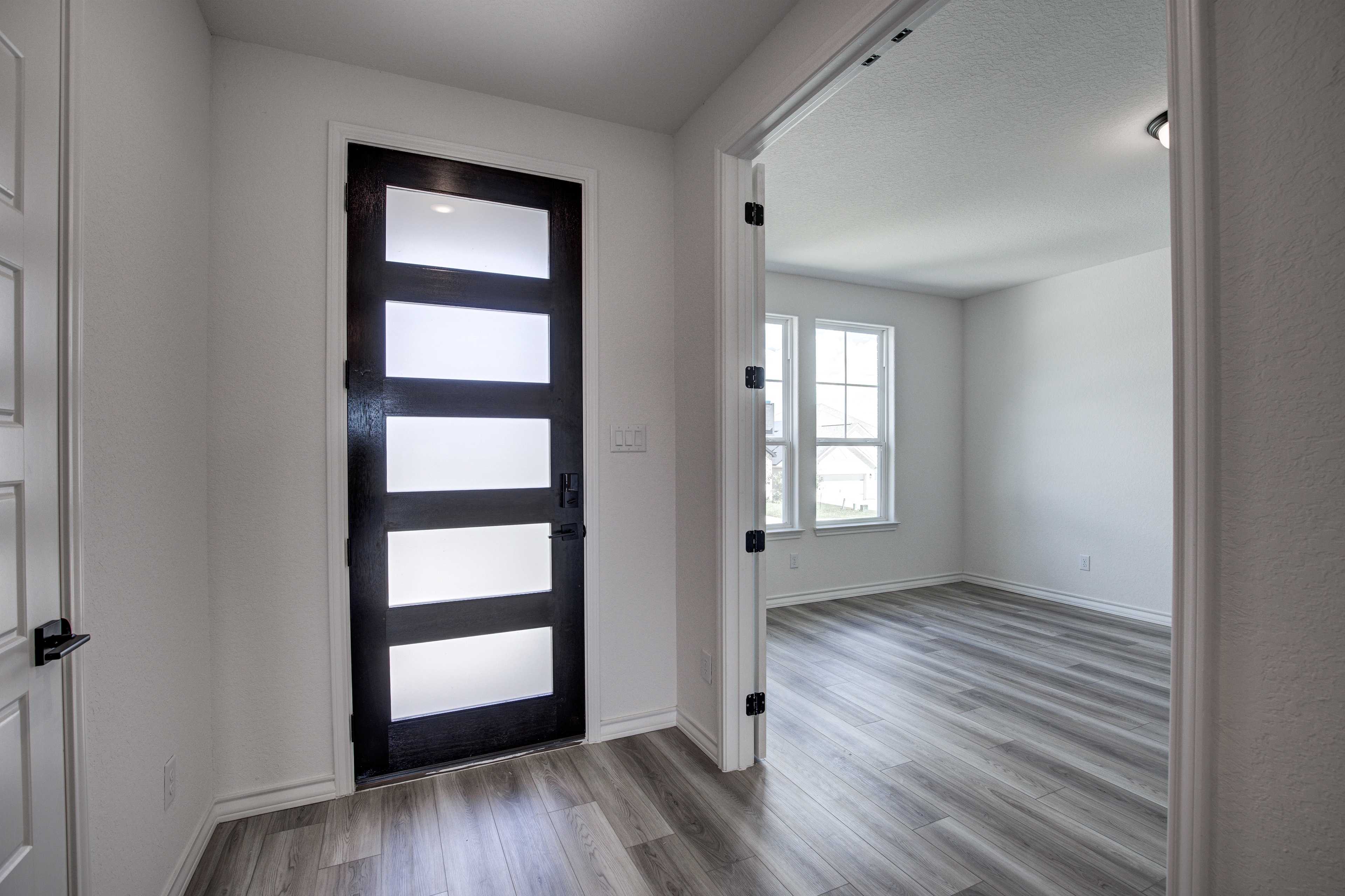 Modern entryway of The Lanier home with black frosted glass door, open archway, white walls, and light wood floors