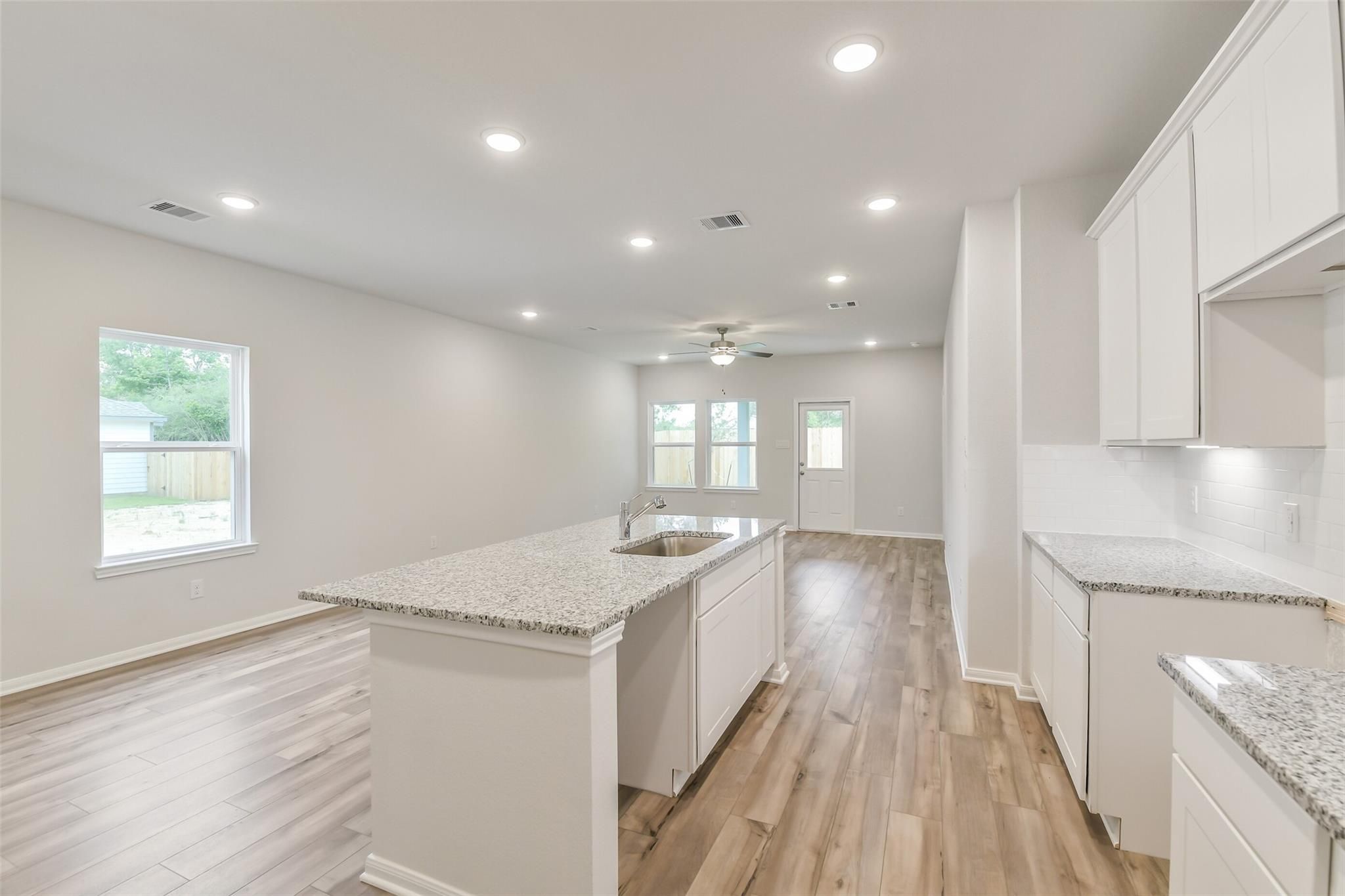 Modern open kitchen featuring white cabinets, granite island sink, hardwood floors in The Brazos F by Davidson Homes, Conroe, TX