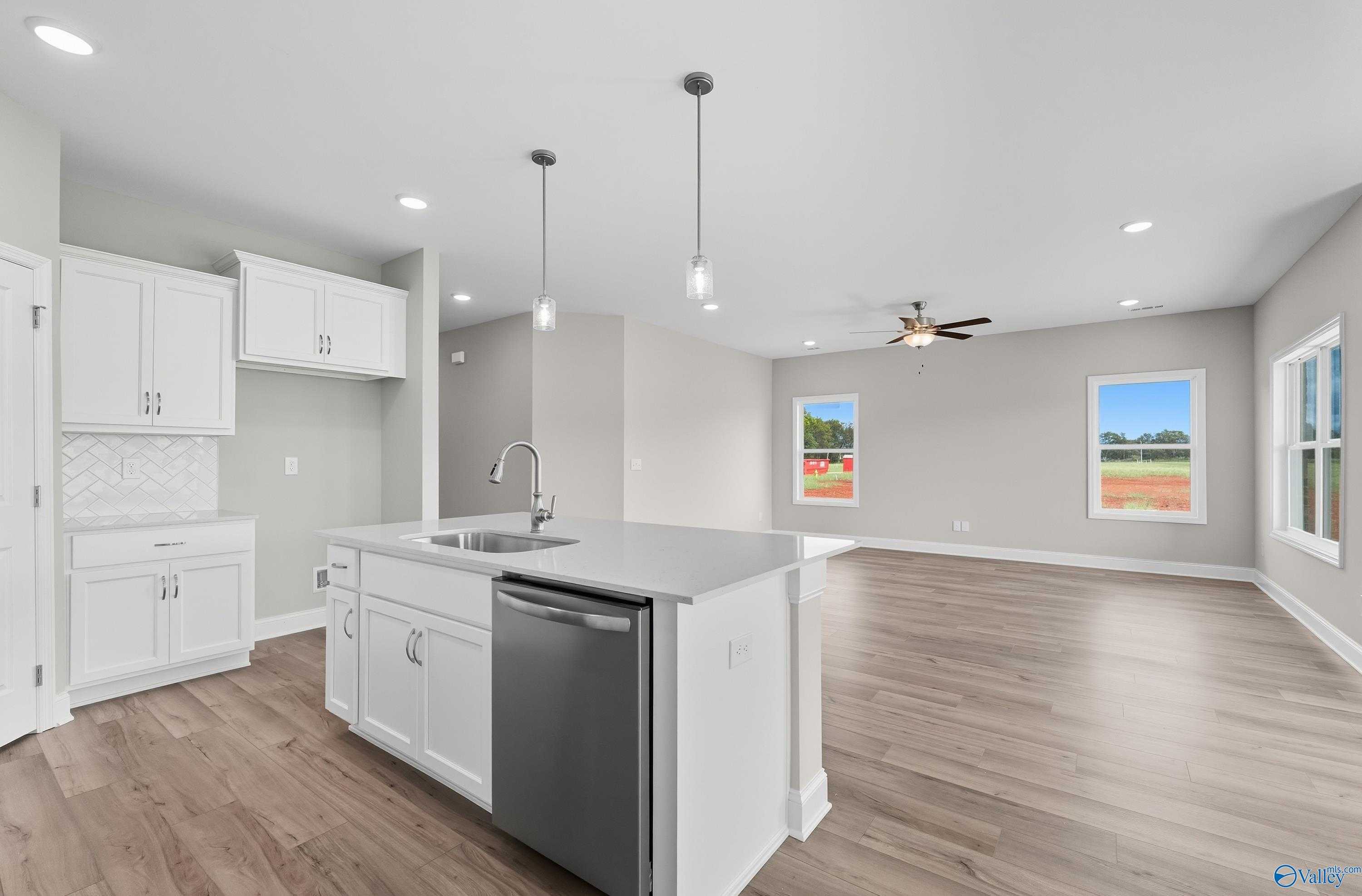 Modern white kitchen island with sink, dishwasher, and pendant lights opening to living room in The Franklin home, Meridianville, AL