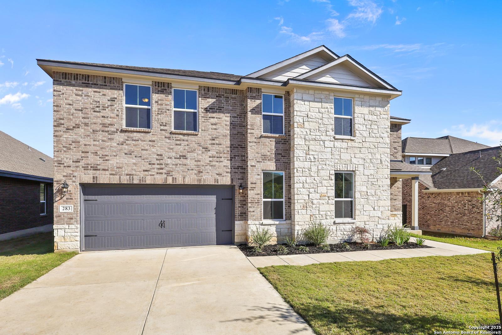 Two-story brick and stone home with 2-car garage, driveway, and lush landscaping in The Reserve at Potranco Oaks, Castroville, Texas