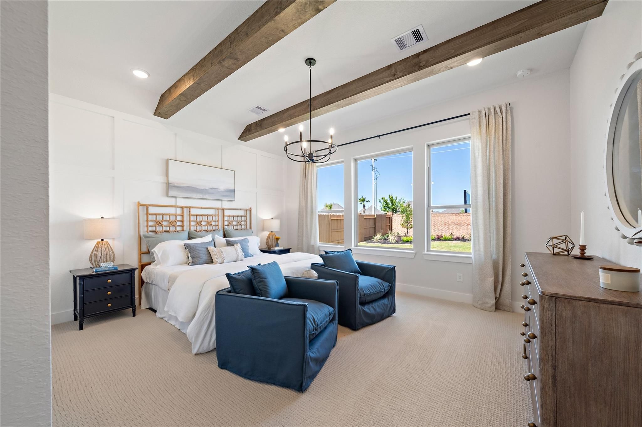 Bright primary bedroom with wood beam ceiling, chandelier, and blue accent chairs in Davidson Homes The Edward A, Lago Mar, Texas City