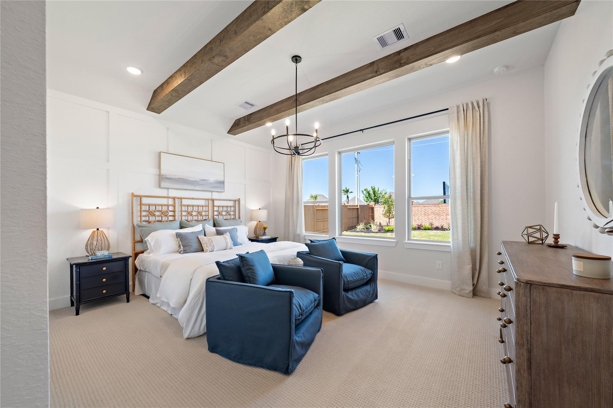 Bright master bedroom with wood beam ceiling, blue accent chairs, and large windows in Davidson Homes The Edward A, Lago Mar, Texas City