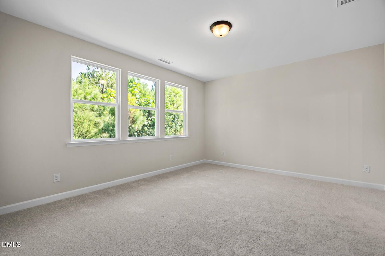Bright spacious bedroom with carpet and three windows overlooking trees in Davidson Homes Birch II C, Sage on North Main, Wake Forest