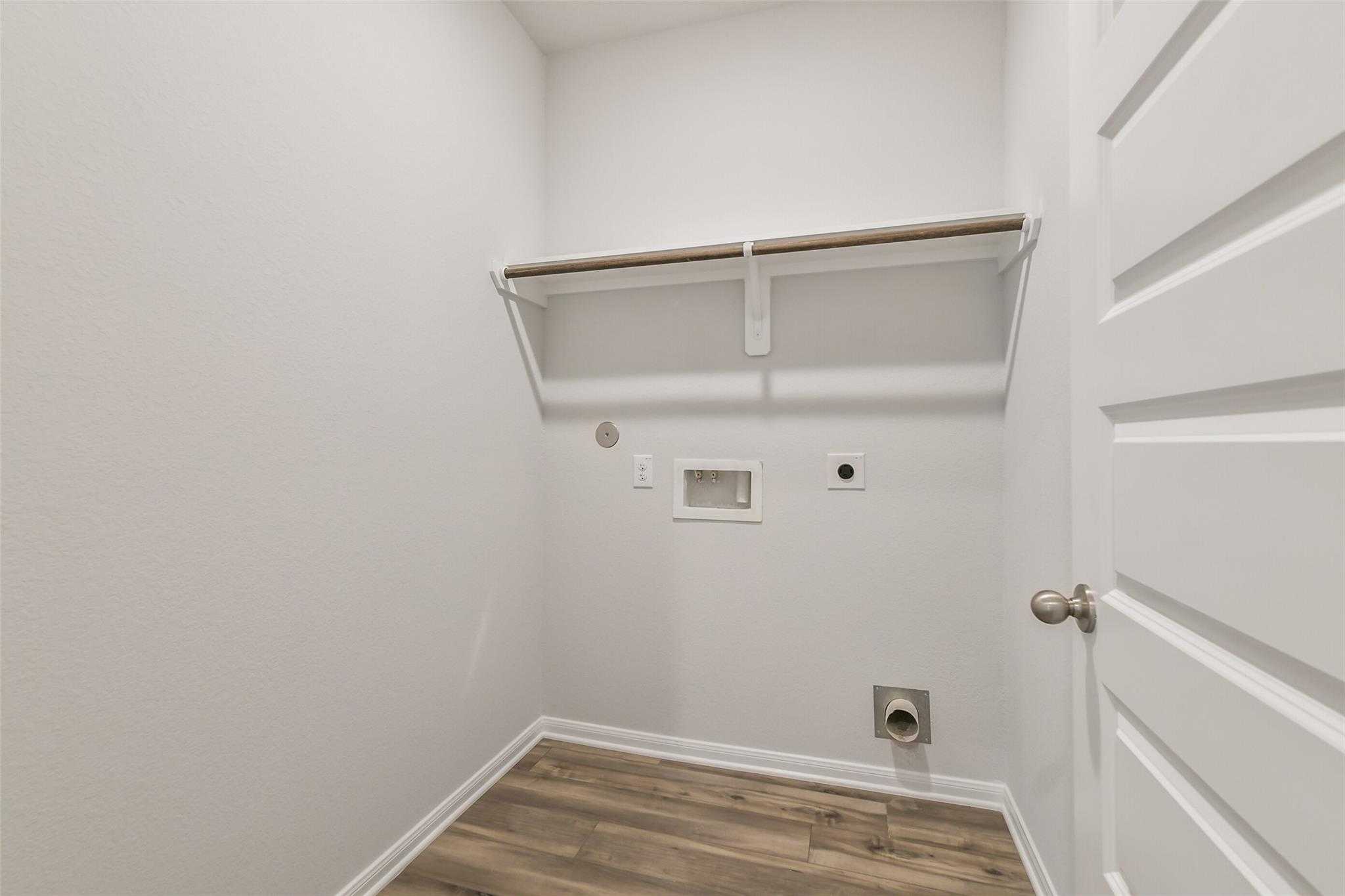 Spacious laundry room with washer/dryer hookups, built-in shelf and wood flooring in Davidson Homes The Brazos F, Conroe, Texas