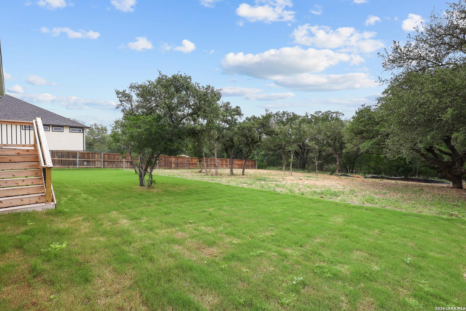Private backyard with lush green lawn, wooden fence, mature oak trees, and deck in Davidson Homes The Belmont H, Potranco Oaks, Castroville, Texas
