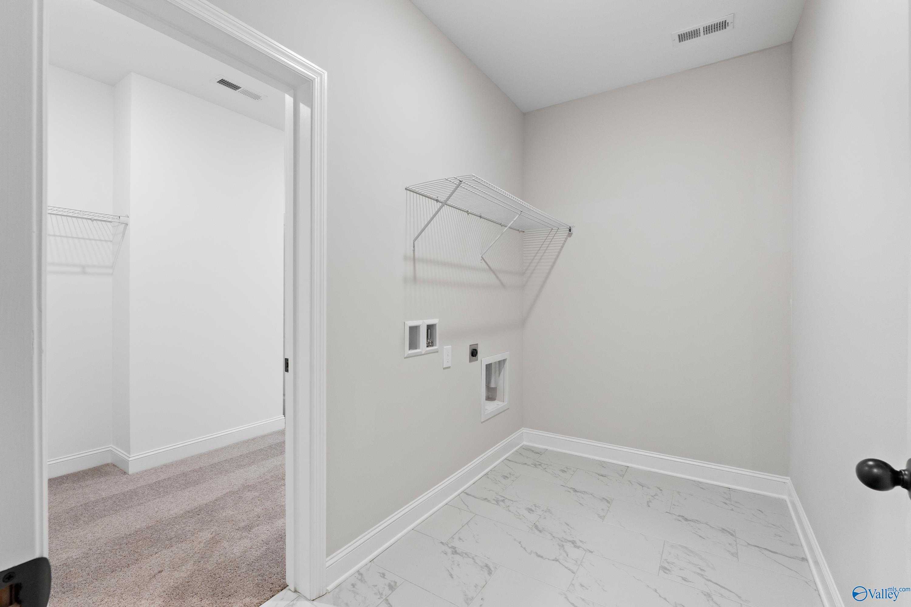 Functional laundry room with open shelving, hanging rods, washer-dryer hookups, and tiled floor in Davidson Homes The Rockford, Toney, Alabama