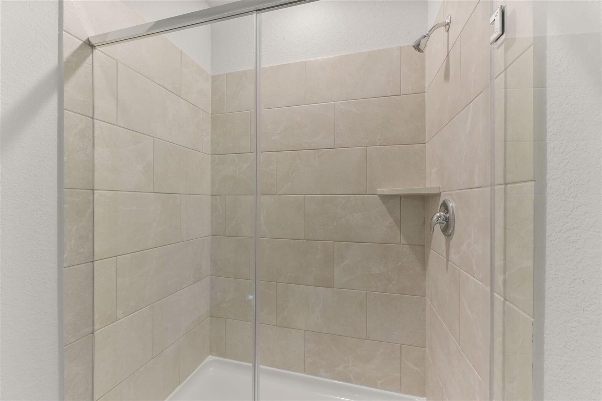 Modern beige subway tile walk-in shower with frameless glass door in Davidson Homes The Laguna B, Magnolia, Texas