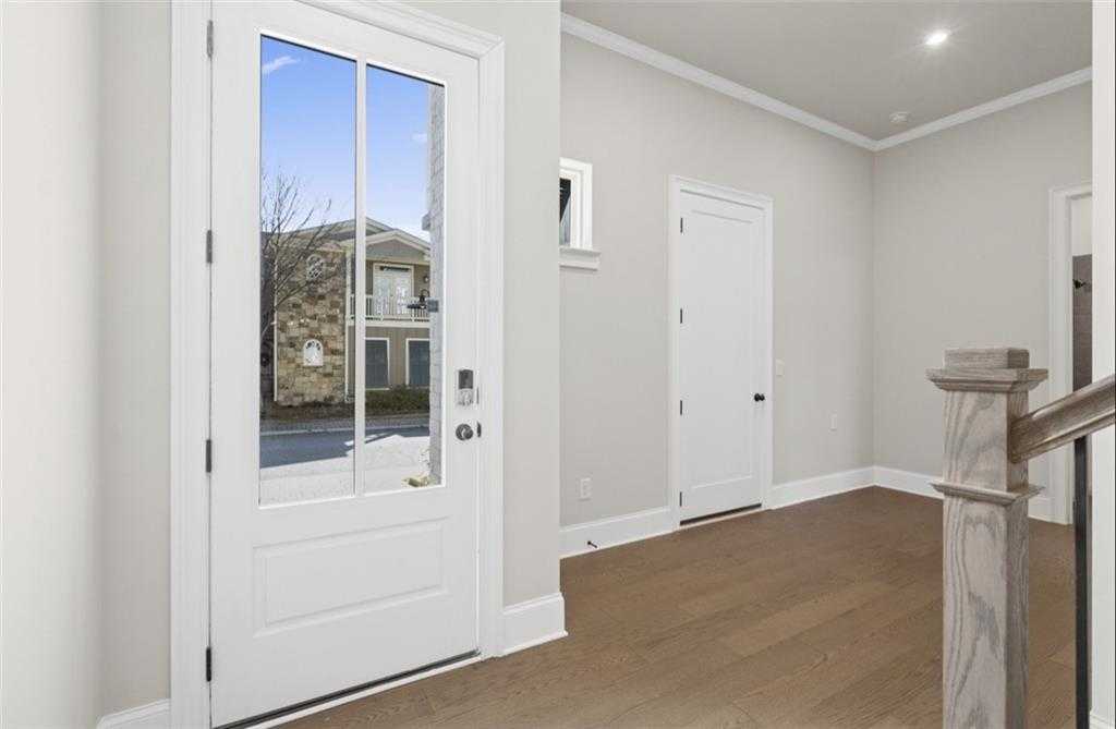 Bright entryway with glass-front door, hardwood floors, and wood staircase in Davidson Homes The Seaside A, Woodstock, GA