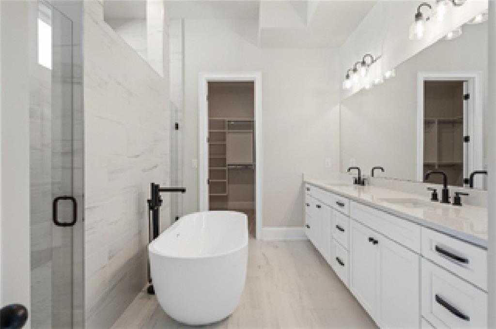 Luxurious master bathroom featuring freestanding white tub, double vanity, glass shower, and walk-in closet in Davidson Homes Seaside A, Woodstock, GA
