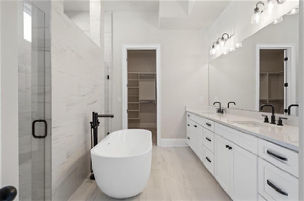 Luxurious master bathroom featuring freestanding white tub, double vanity, glass shower, and walk-in closet in Davidson Homes Seaside A, Woodstock, GA