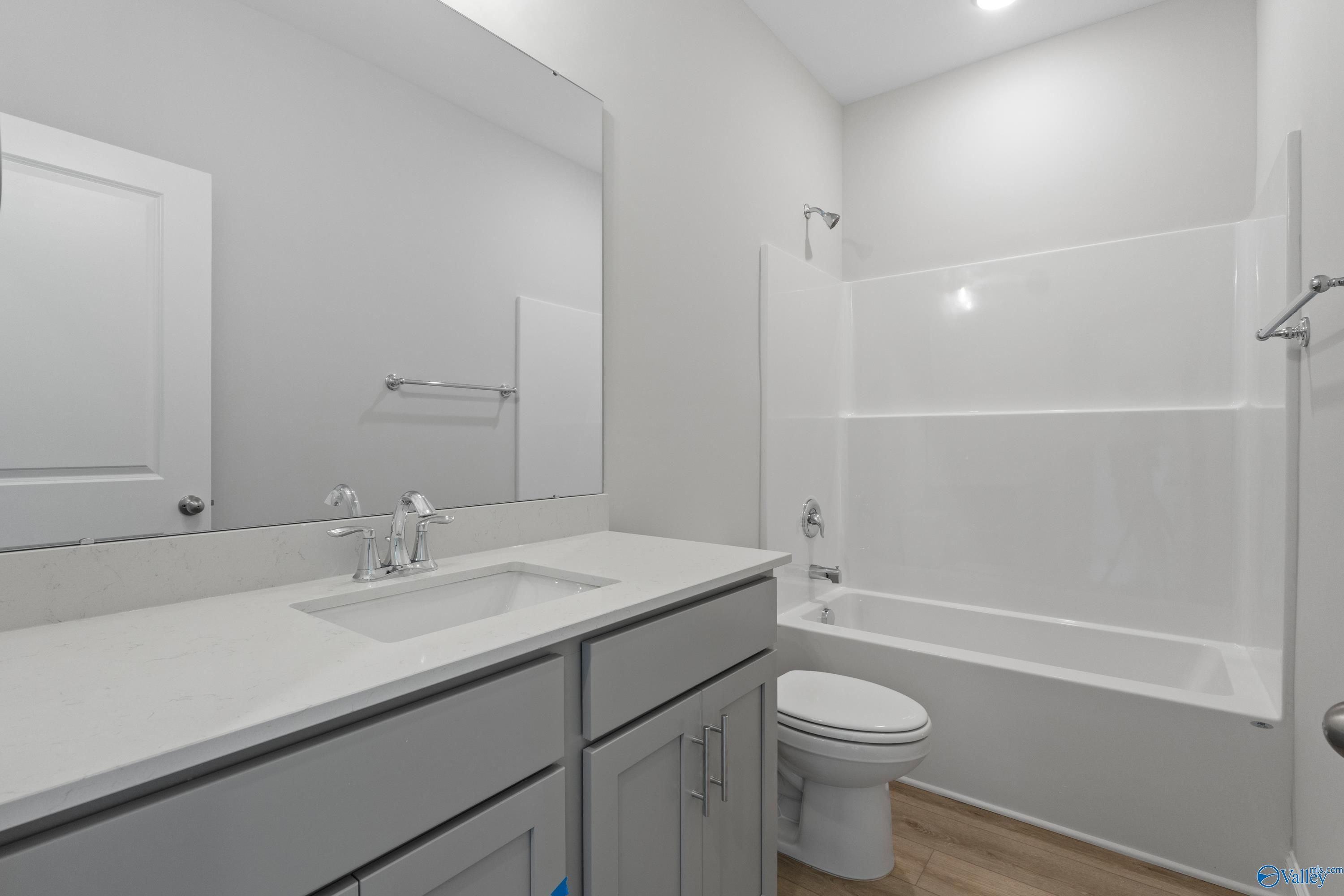 Bright bathroom with white tub-shower combo, quartz double vanity, mirror, and wood floors in The Asheville 3-bedroom home, Huntsville, Alabama