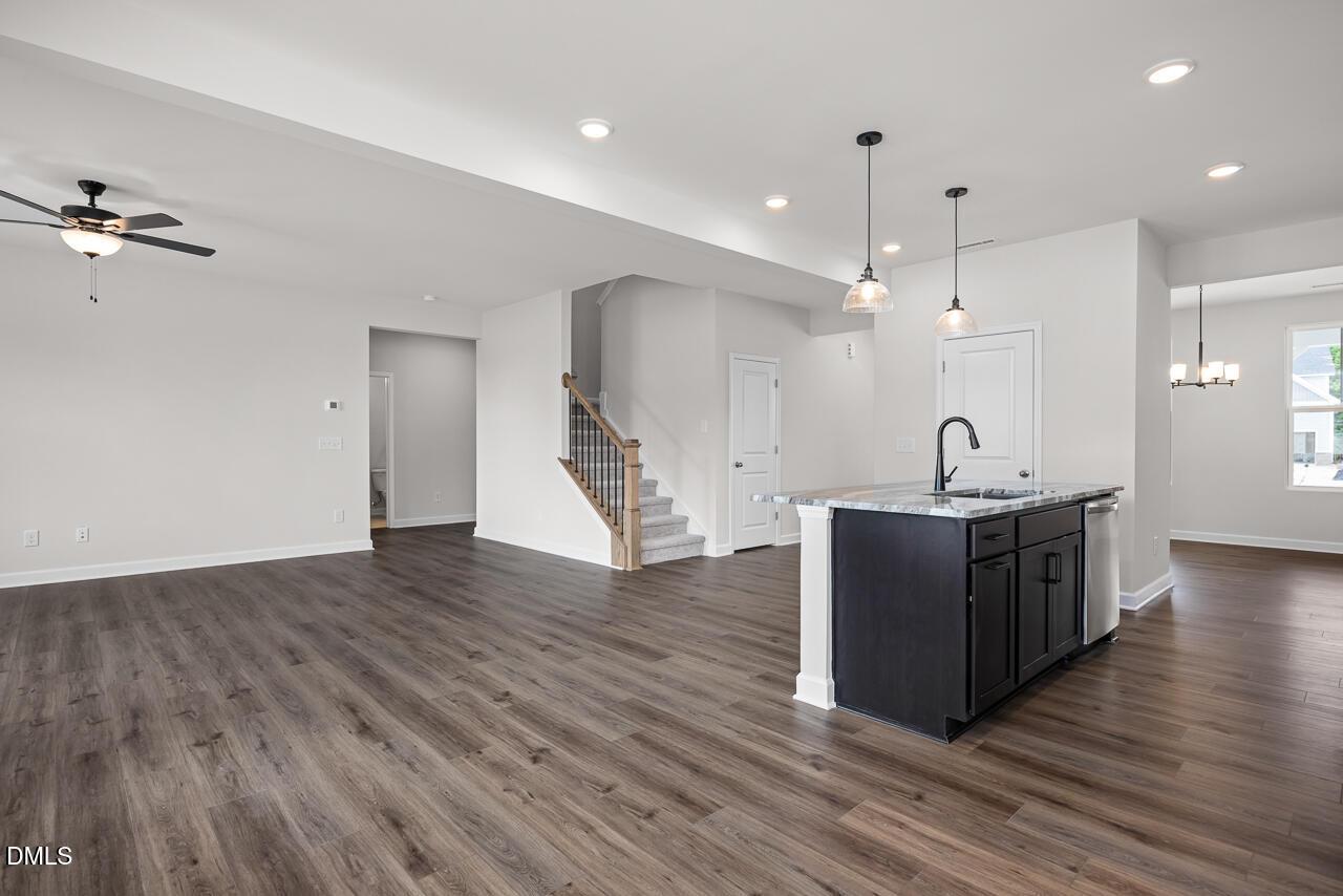Open-concept kitchen and living area with dark island, wood-look floors, and staircase in Willow B home, Zebulon, NC.