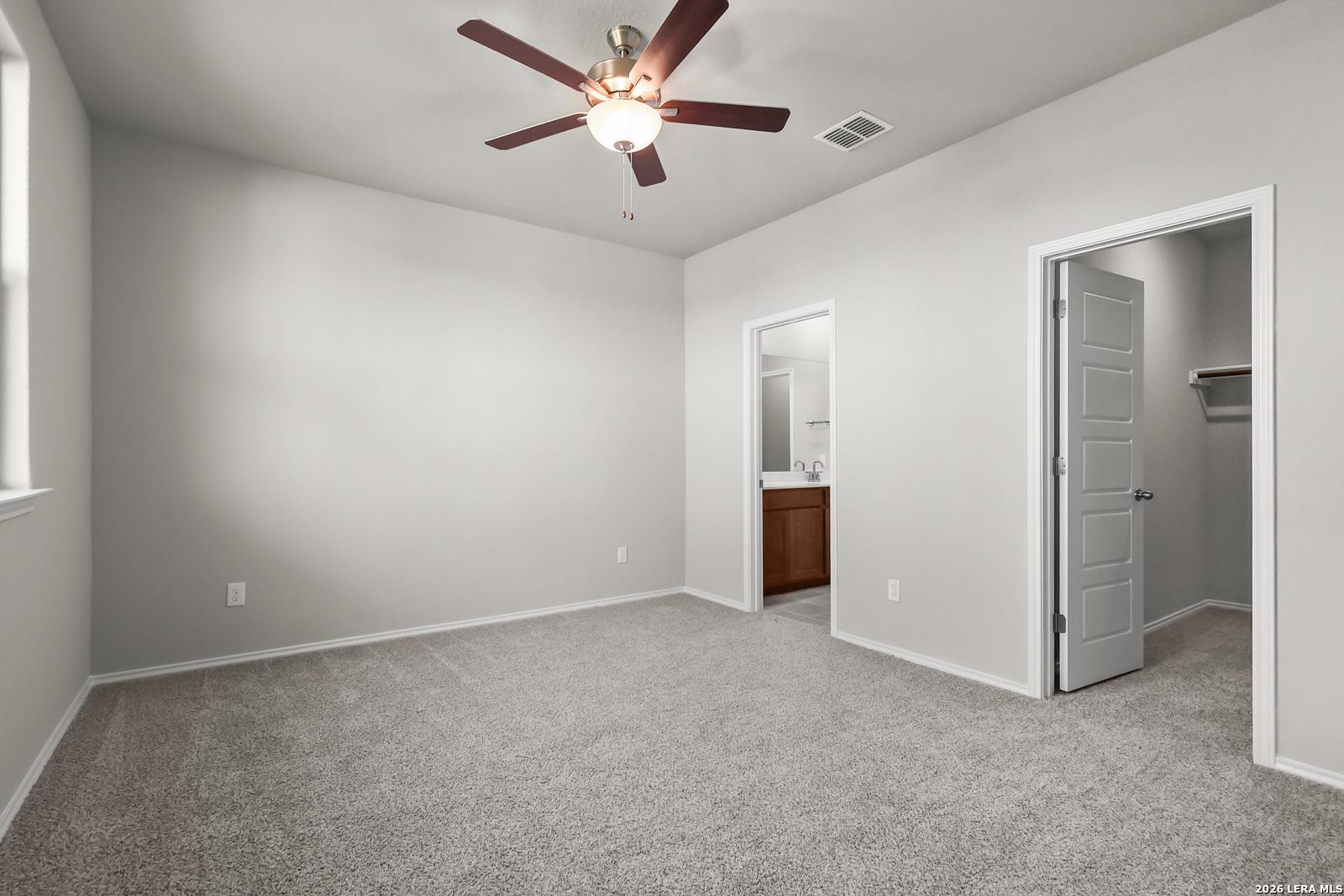 Bright secondary bedroom with gray carpet, ceiling fan, adjacent bath, and walk-in closet in Davidson Homes The Frio B, San Antonio