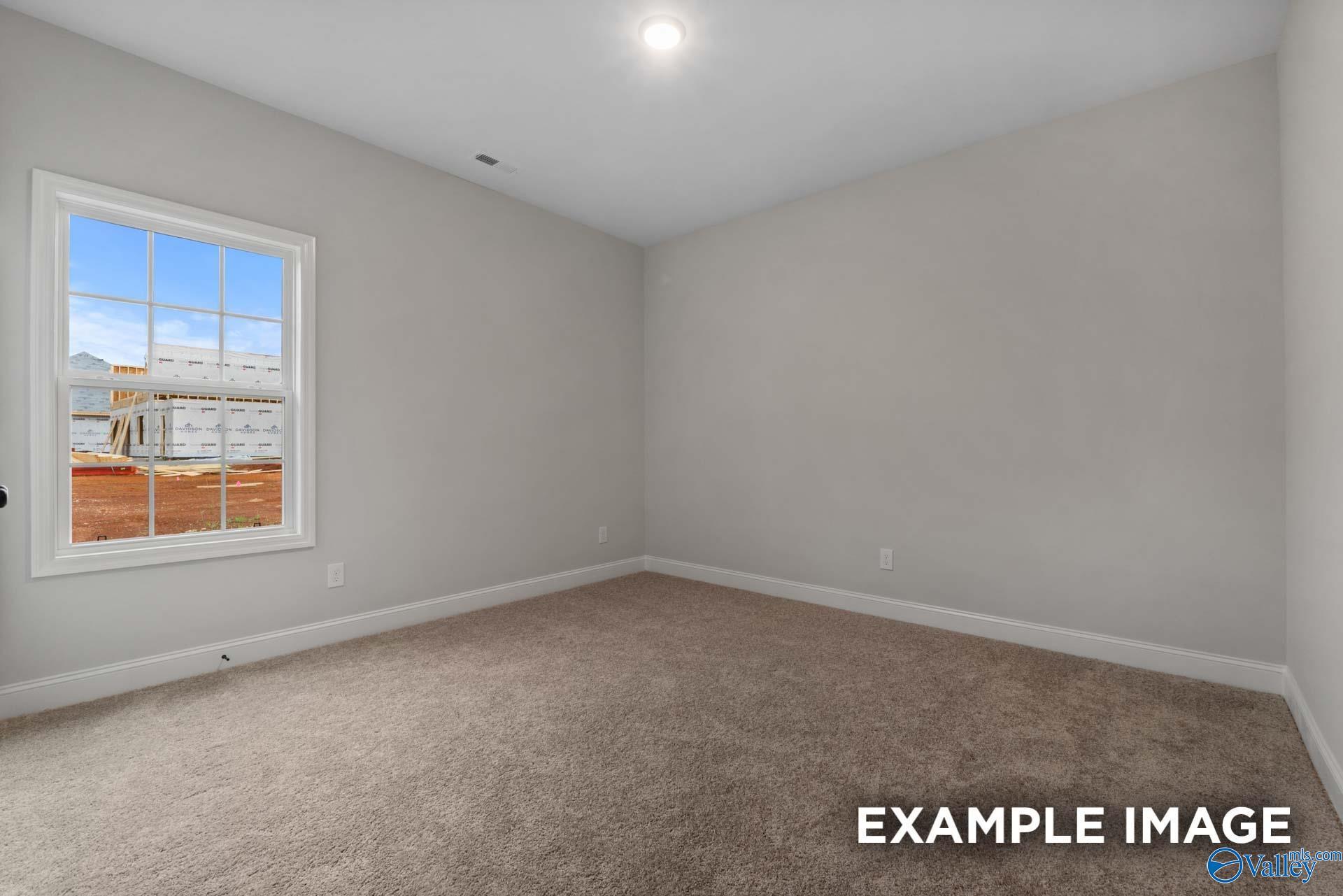 Bright empty secondary bedroom with light gray walls, beige carpet, and large window in Davidson Homes The Finleigh, Meridianville, Alabama