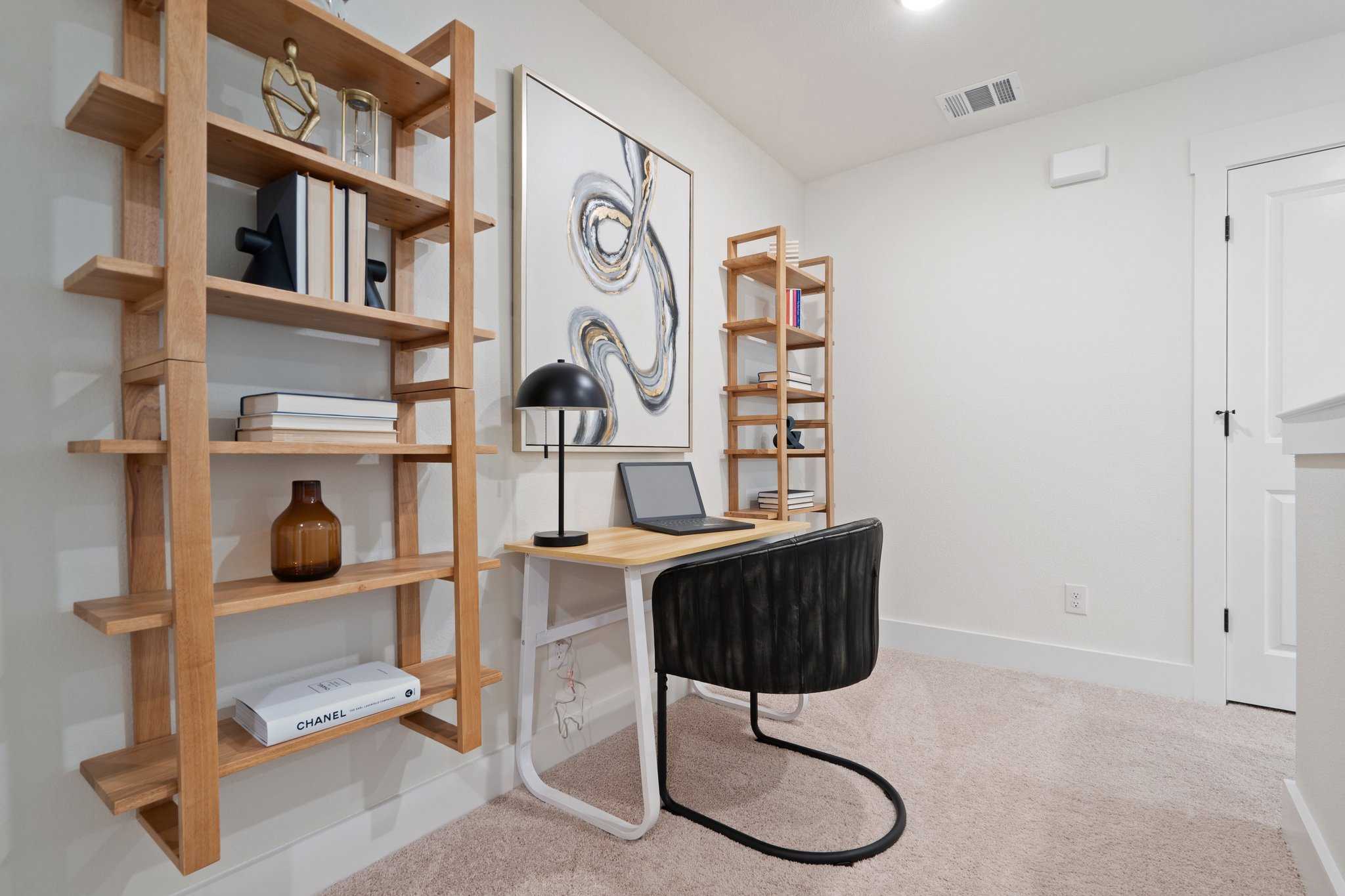 Modern home office in The Wake by Davidson Homes featuring wooden bookshelves, abstract wall art, and sleek desk with laptop