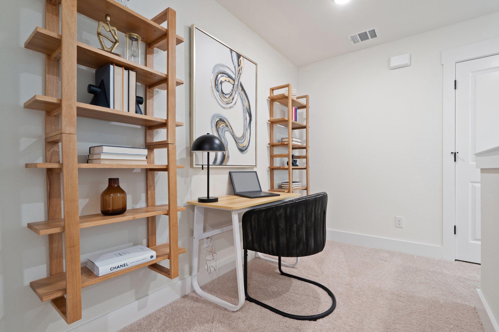 Modern home office in The Wake C featuring open wooden shelves, abstract art, sleek desk with laptop, and black accent chair