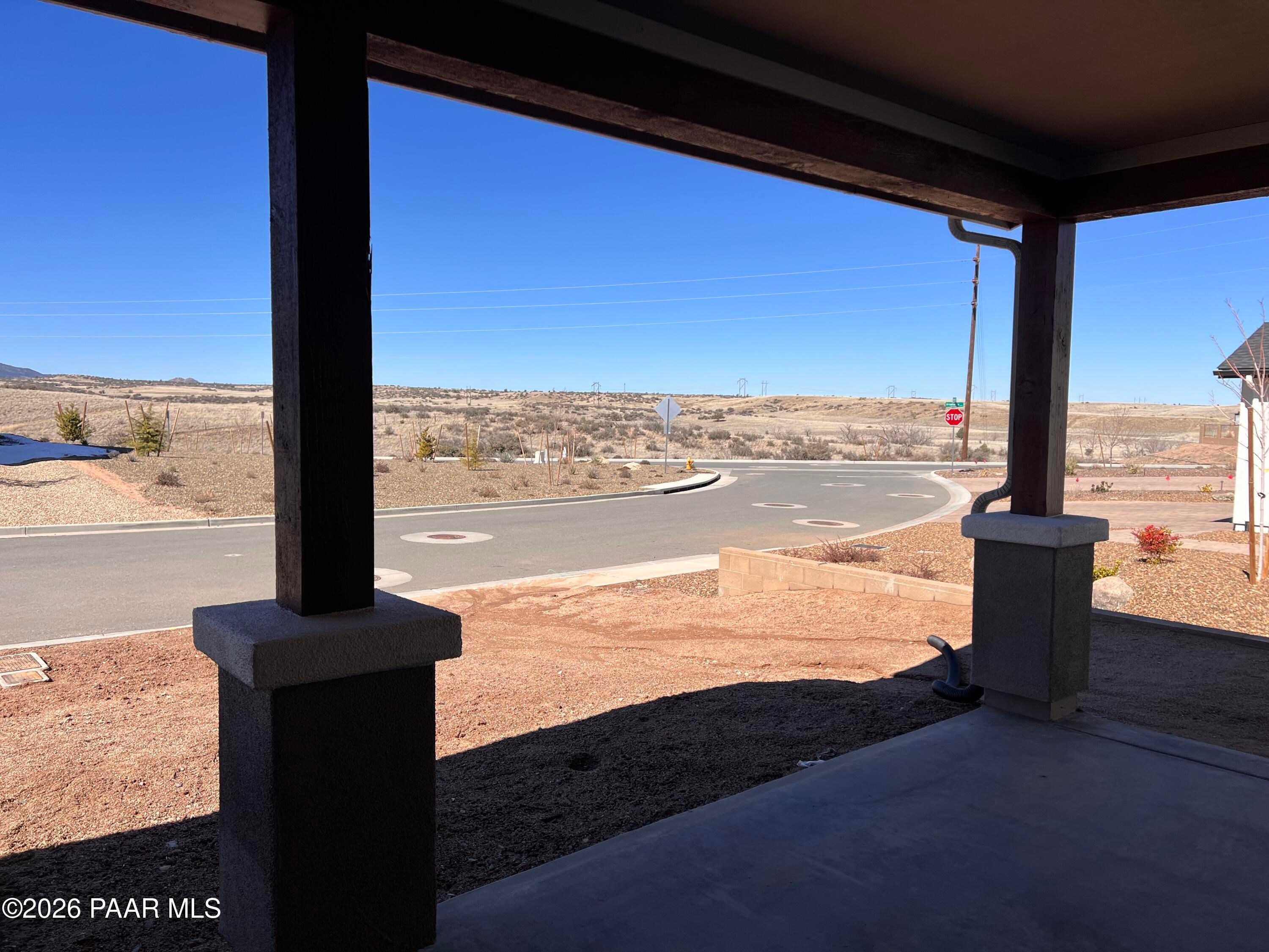 Covered patio with wooden beams overlooking curved driveway and desert landscape in Davidson Homes Sunrise II A, Prescott AZ