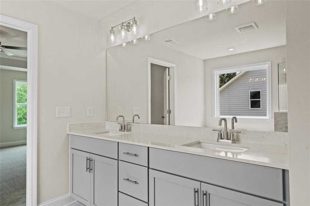 Elegant double vanity with quartz countertop, gray cabinets, and large mirror in master bath of The Hickory B at Wehunt Meadows, Hoschton, Georgia