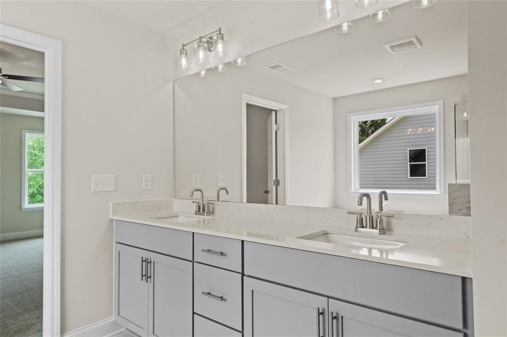 Elegant double vanity with quartz countertop, gray cabinets, and large mirror in master bath of The Hickory B at Wehunt Meadows, Hoschton, Georgia