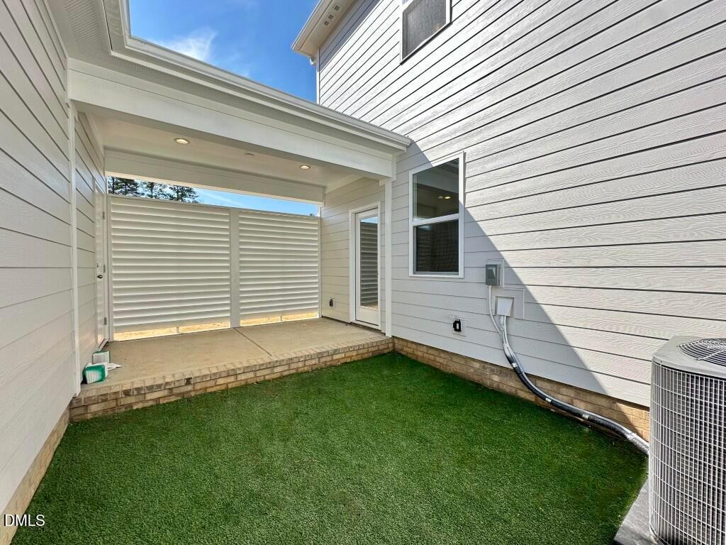 Covered patio with white siding, glass door, shutters, and artificial turf yard in Davidson Homes The Burke, Knightdale, NC