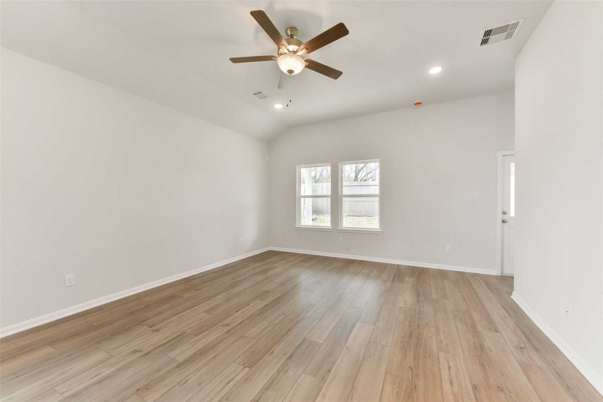 Spacious living room with light gray walls, hardwood floors, large windows, ceiling fan in Davidson Homes The Laguna B, Magnolia, Texas