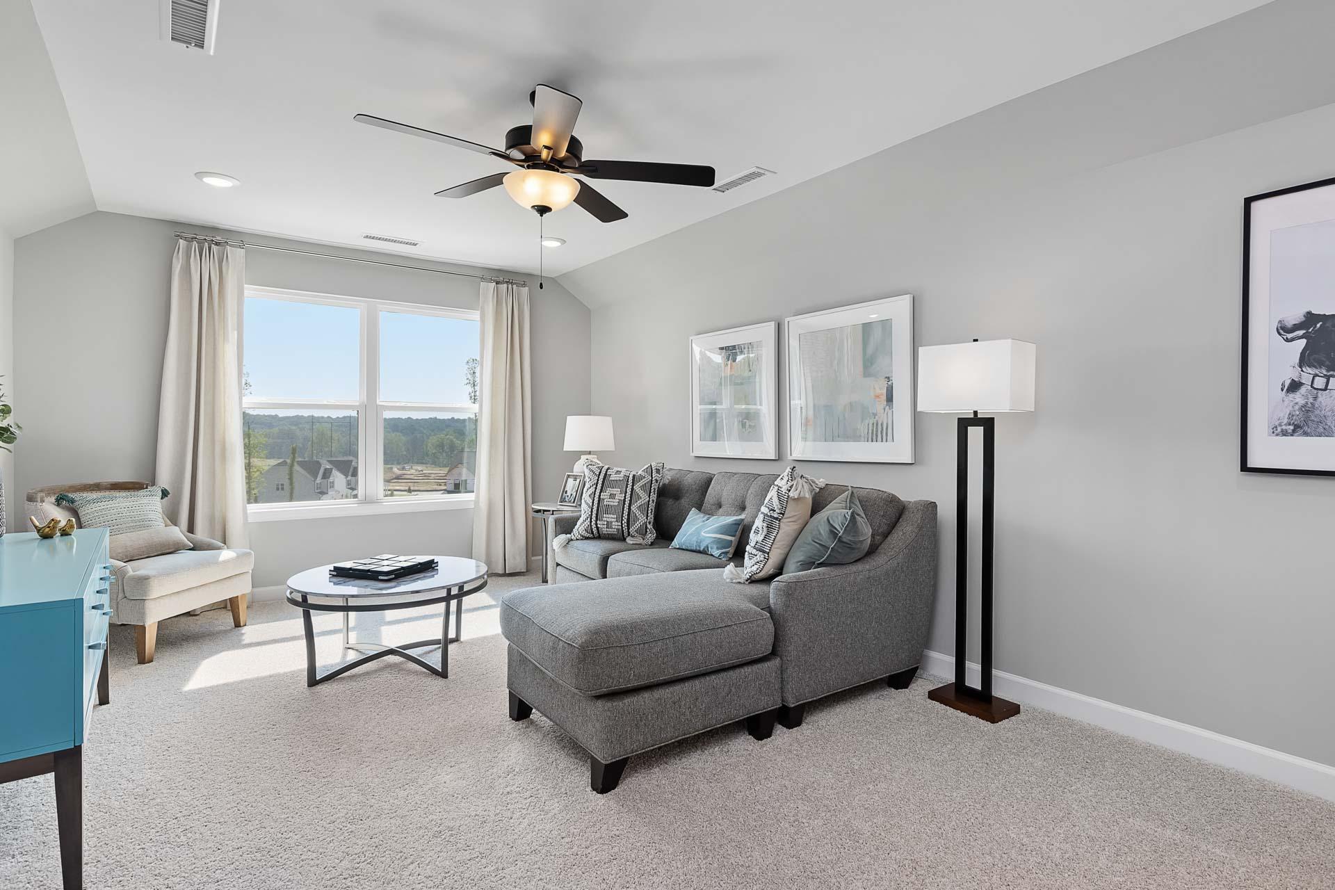 Spacious bonus room in Highland Forest Fuquay-Varina NC with gray L-shaped sofa, large windows, and modern decor