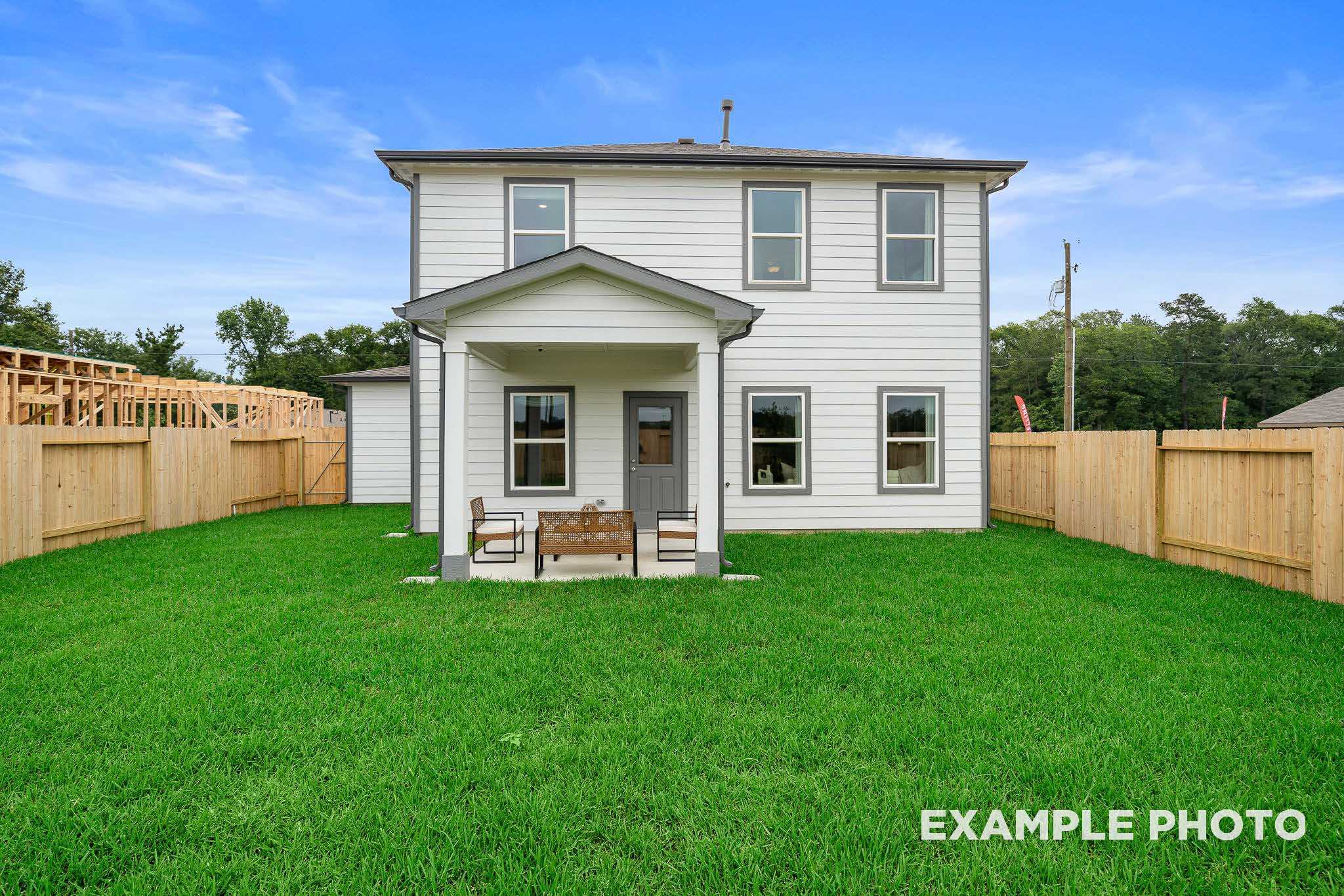 Rear view of The Trinity F two-story home with white siding, covered porch, large windows, green lawn, and wooden fence in Beasley, Texas