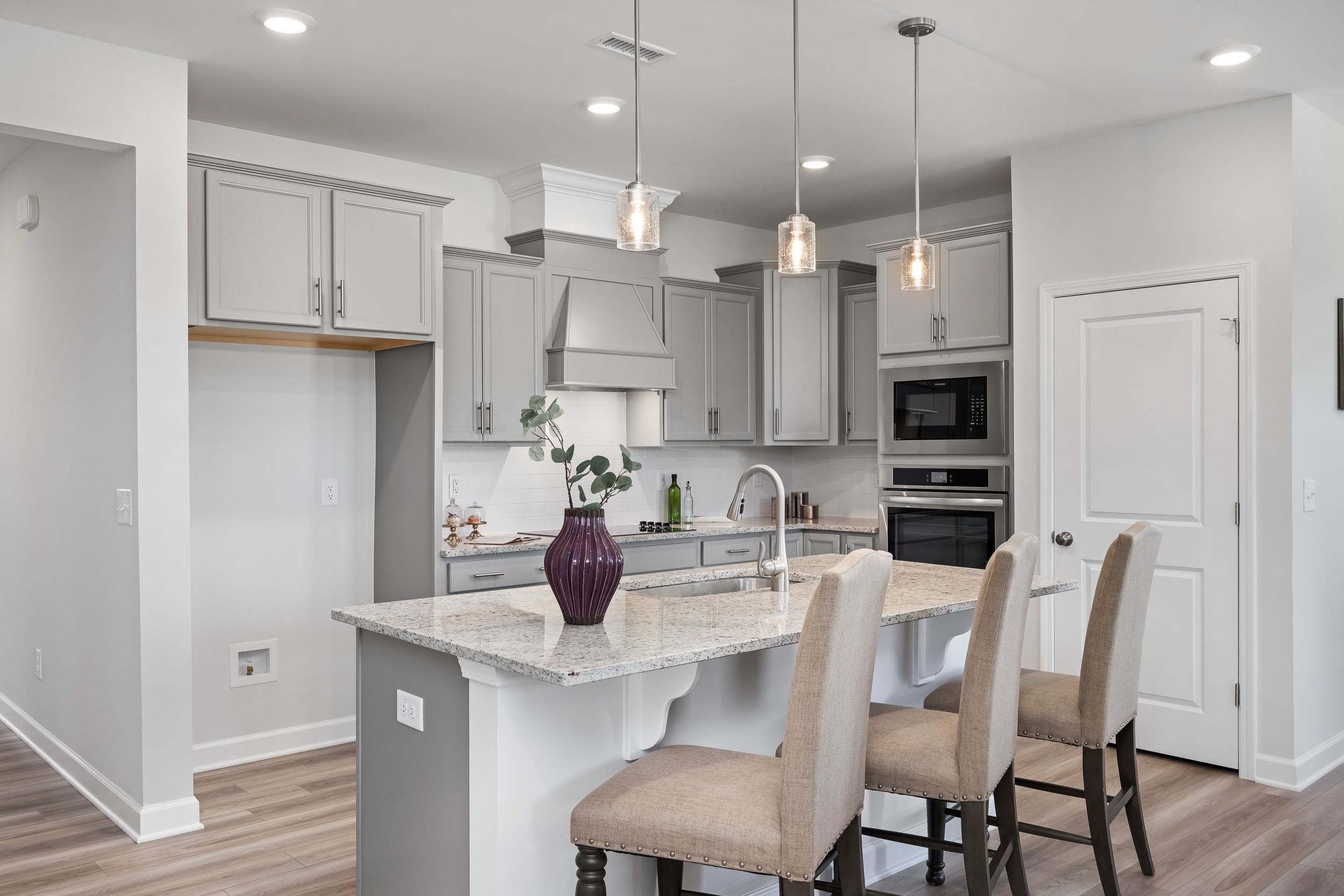Modern kitchen in The Daphne C home by Davidson Homes featuring gray cabinets, quartz island with bar stools, stainless appliances, pendant lights