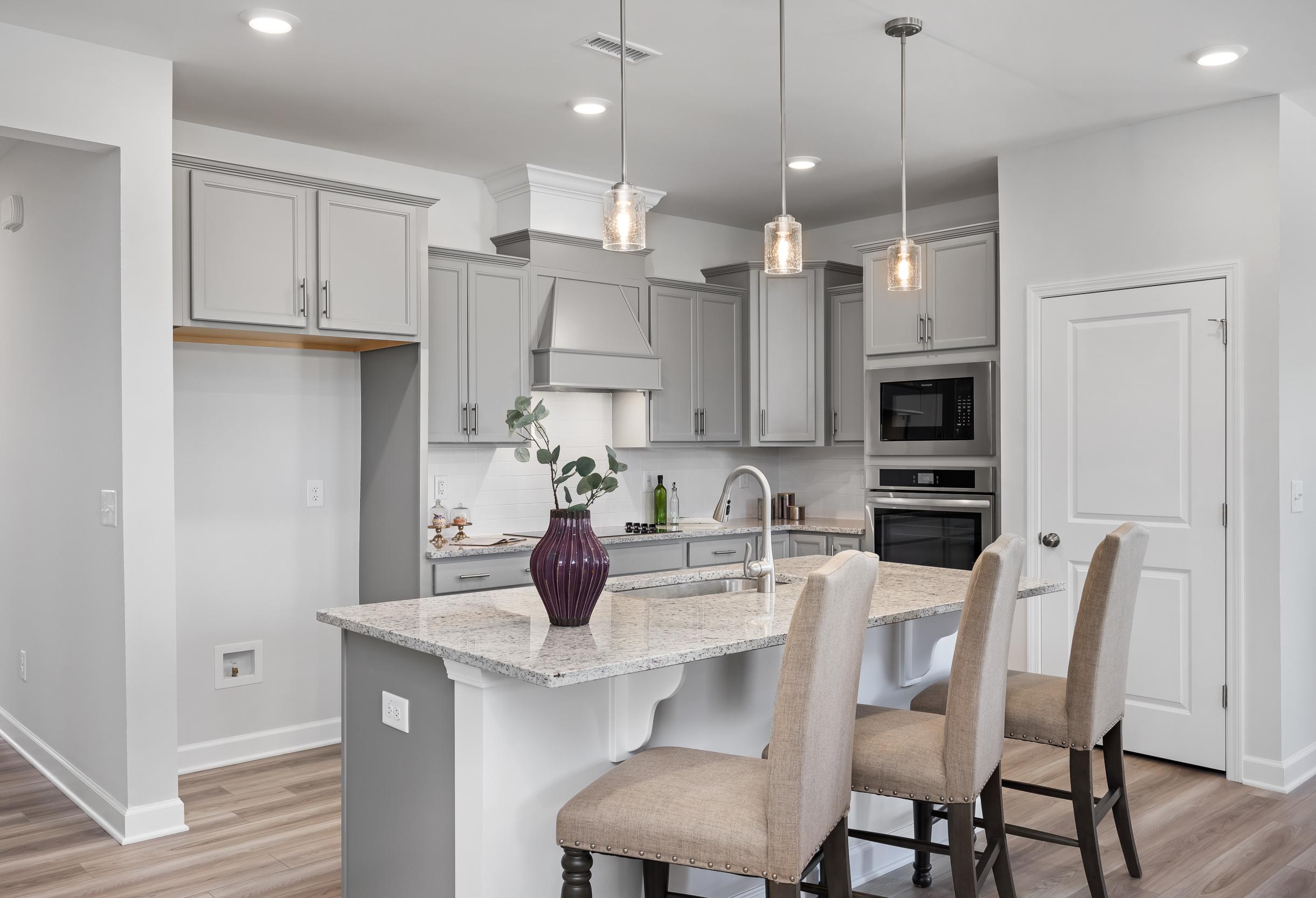 Modern kitchen in The Daphne C home by Davidson Homes featuring gray cabinets, quartz island with bar stools, stainless appliances, pendant lights