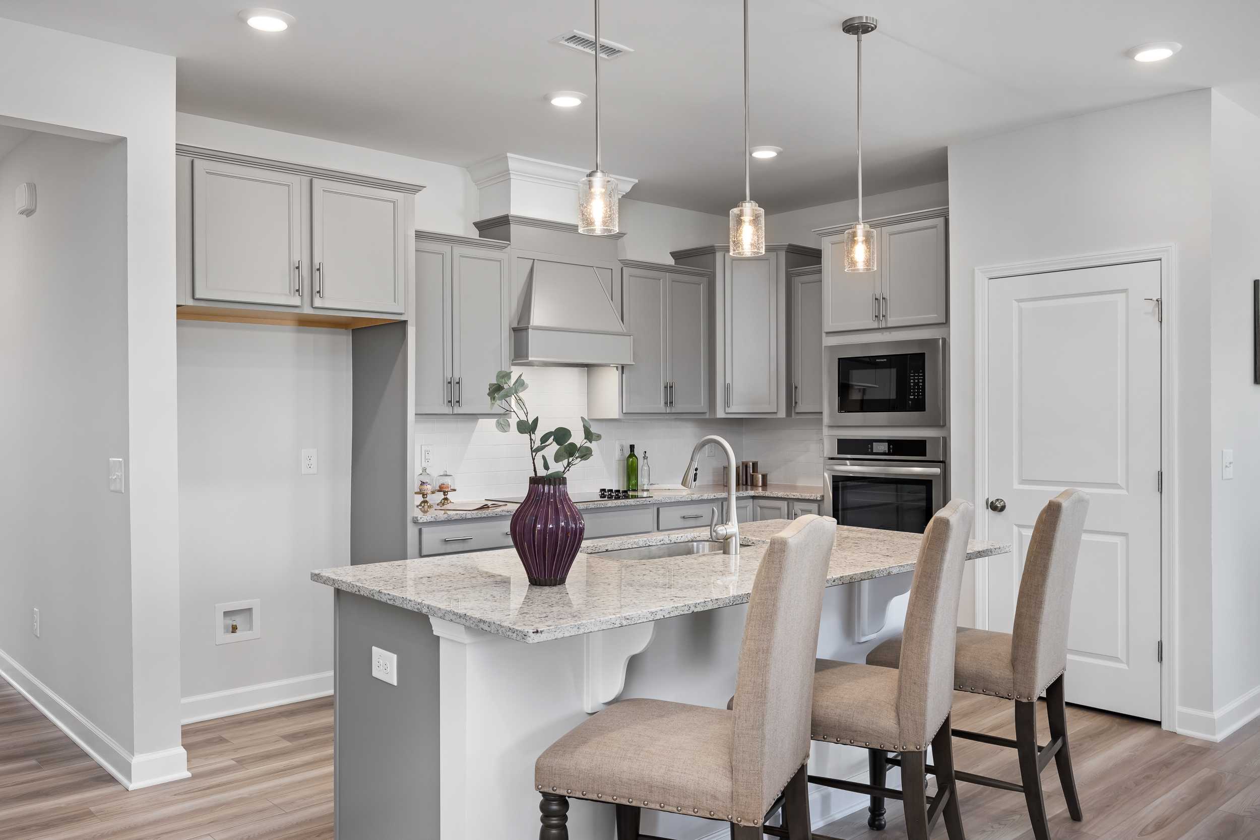 Modern kitchen in The Daphne C home by Davidson Homes featuring gray cabinets, quartz island with bar stools, stainless appliances, pendant lights