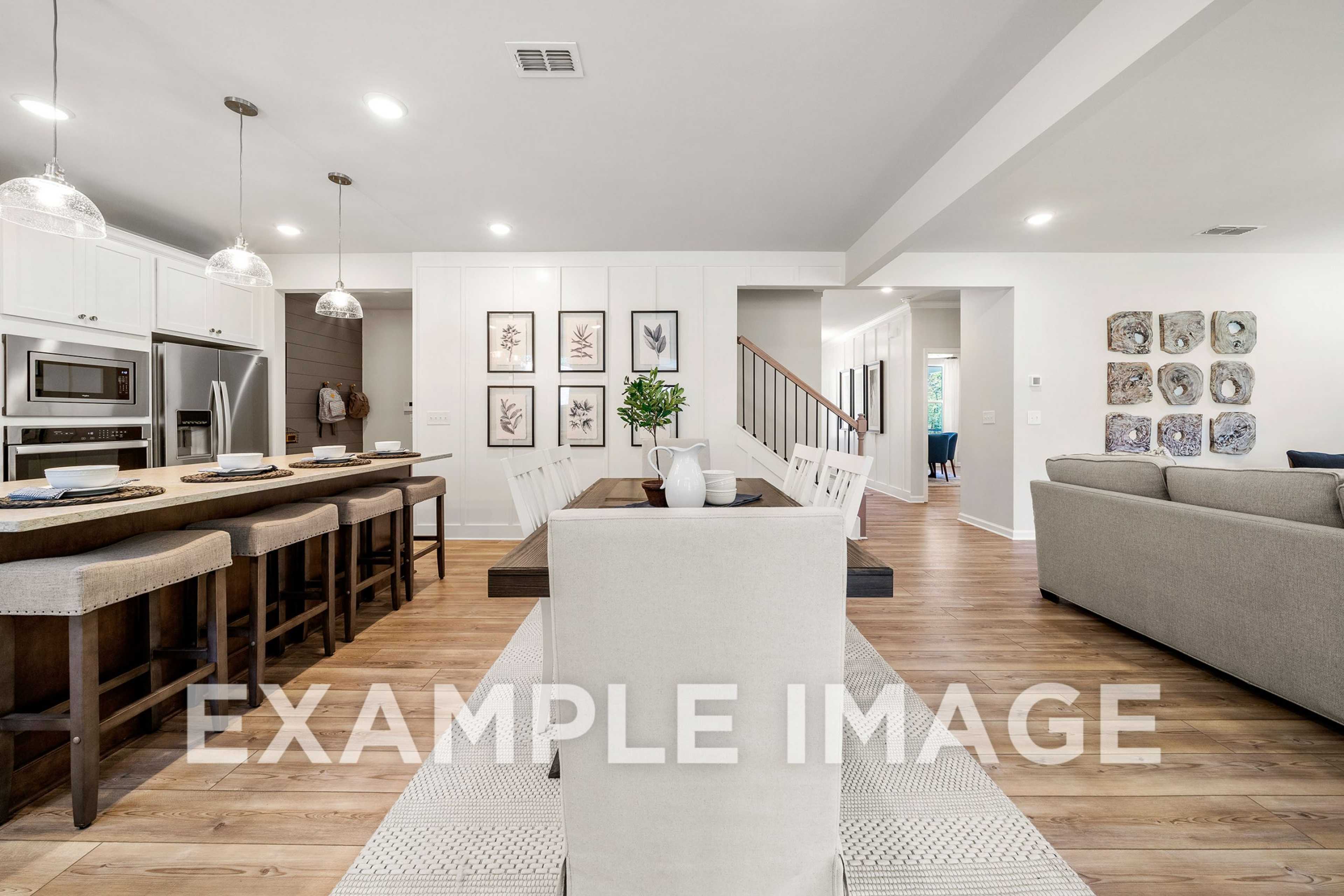 Open-concept kitchen and living area in The Hickory A featuring white cabinetry, large island, dining table, and gray sofa
