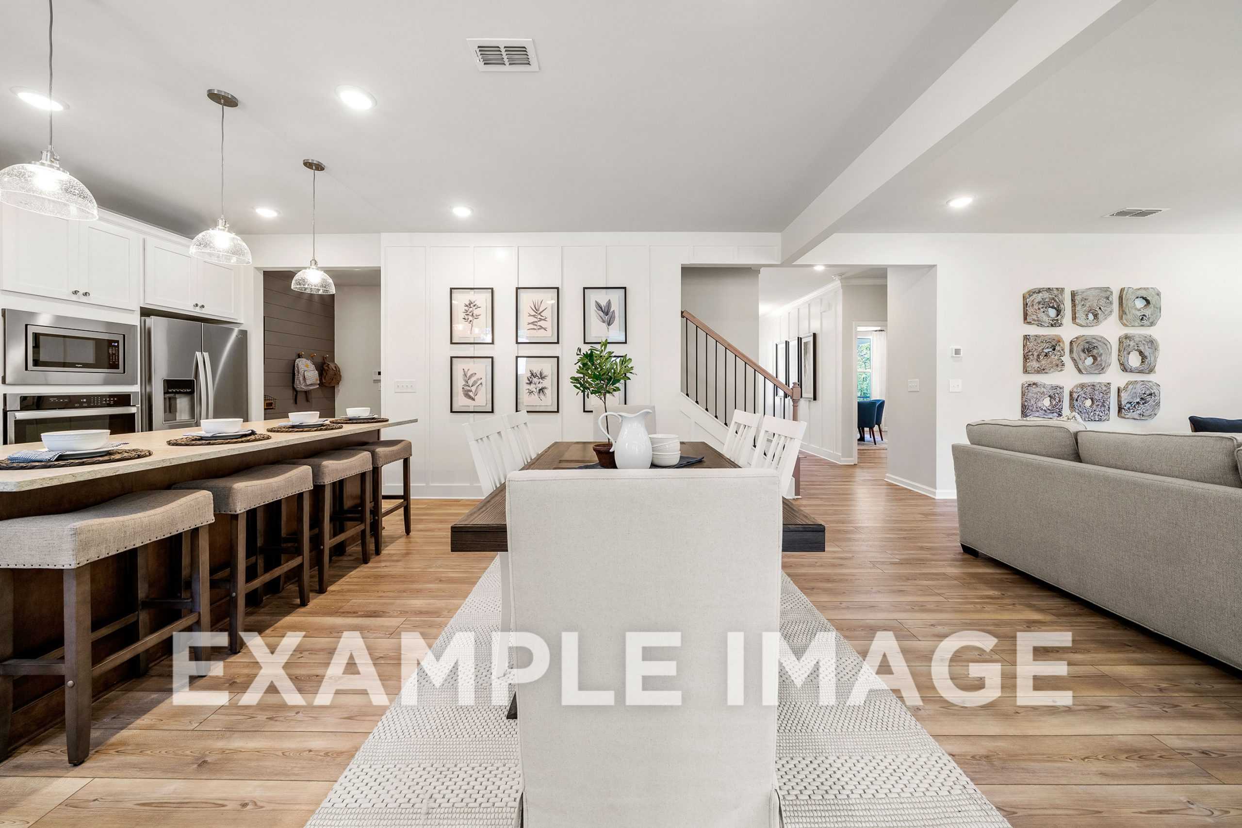Open-concept kitchen and living area in The Hickory A featuring white cabinetry, large island, dining table, and gray sofa