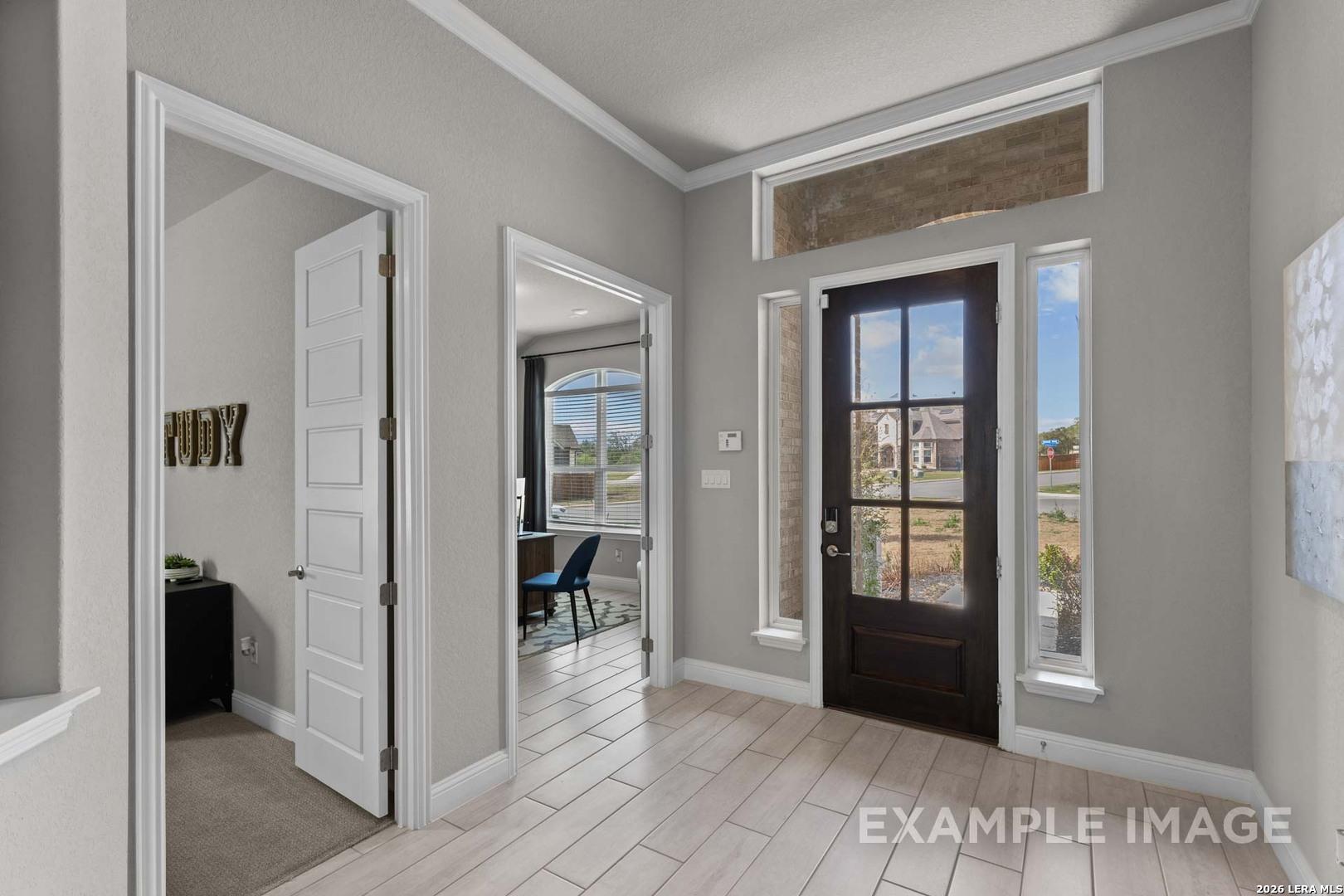 Bright entryway with wood-style tile floors and glass-paneled front door in The Garner C floor plan, Castroville, Texas.