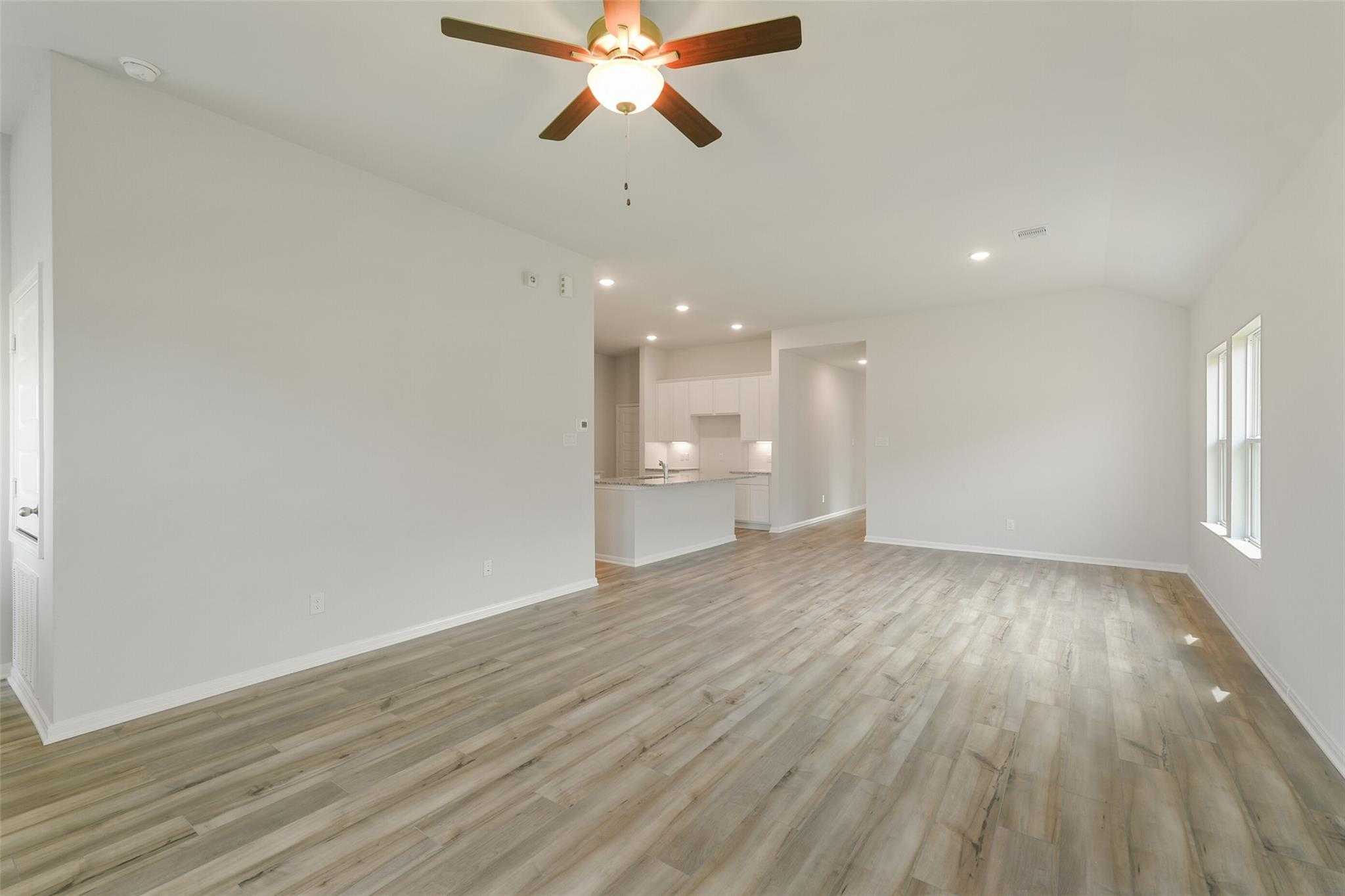 Open-concept living room with light wood floors, ceiling fan, and white kitchen view in Davidson Homes The Laguna B, Dayton Texas