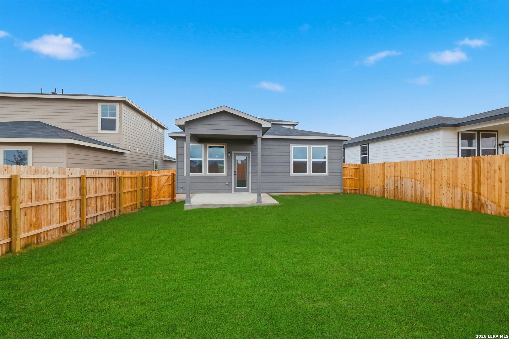 Gray two-story home with covered patio, large windows, and lush green backyard fenced in wood, Agave San Antonio Texas Davidson Homes Blanco C