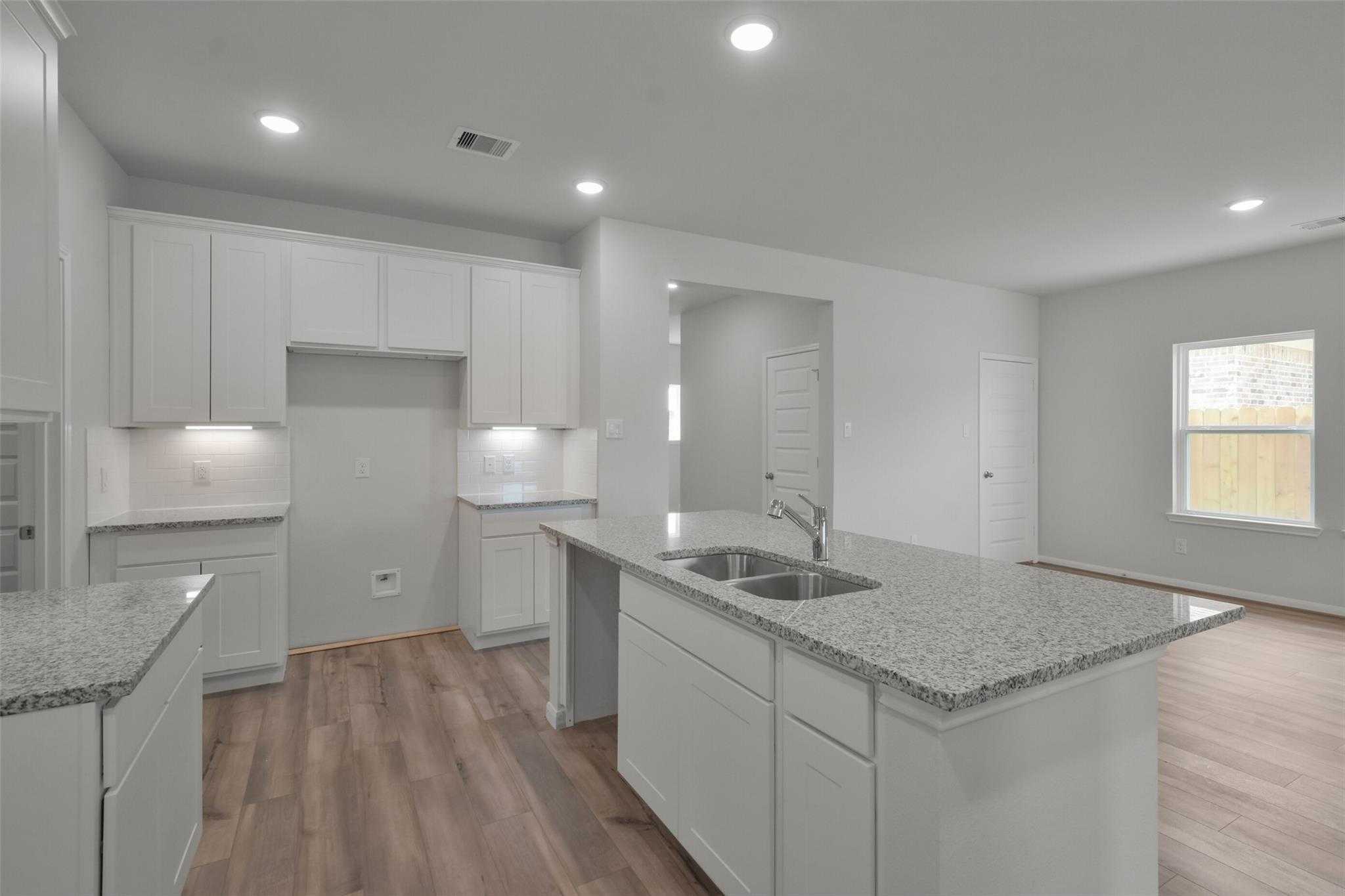Spacious modern kitchen with white cabinets, granite island sink, and open layout in Davidson Homes The Tierra A, Dayton, Texas