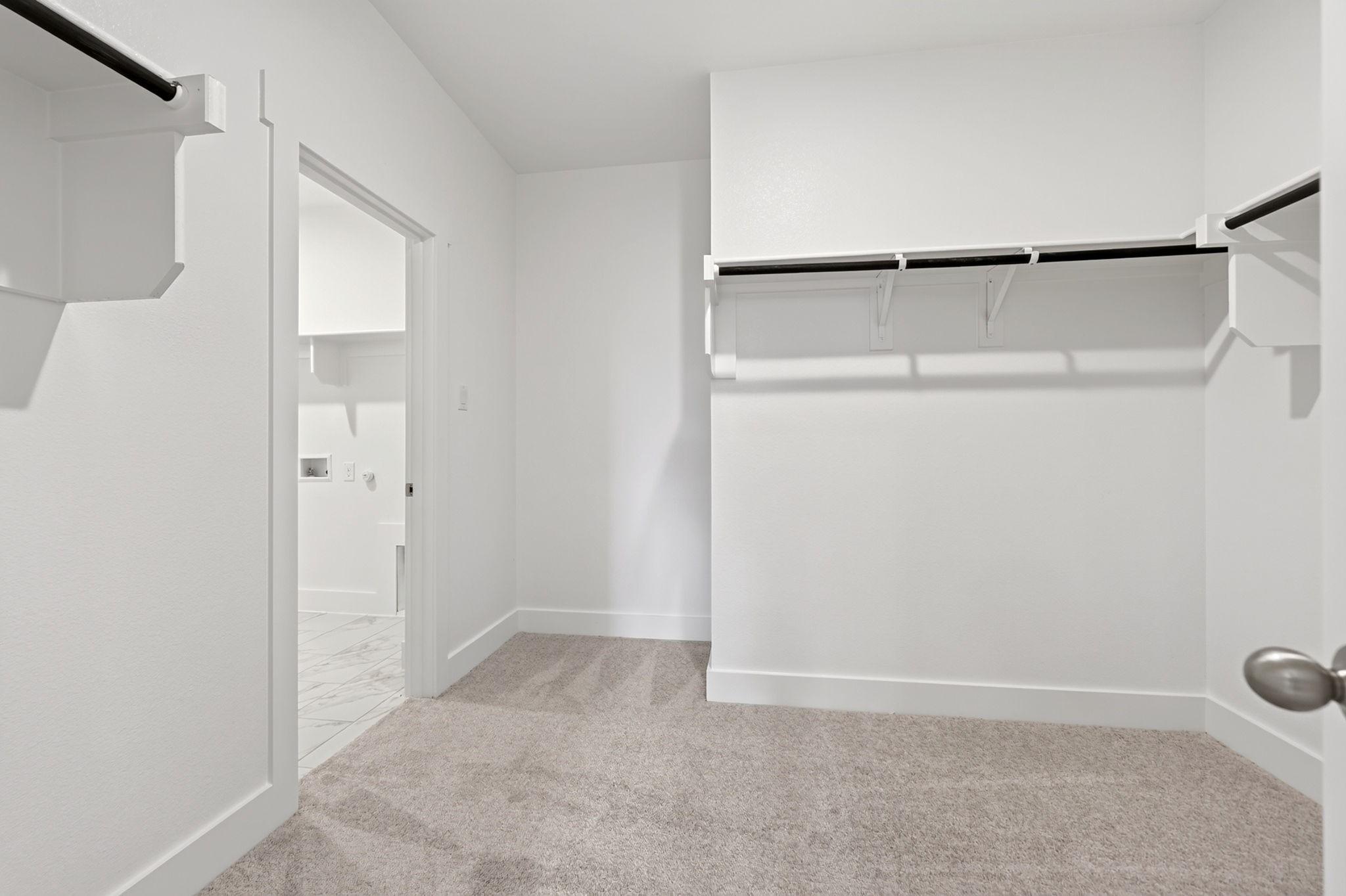 Spacious walk-in closet with hanging rods and carpet flooring connecting to laundry room in Davidson Homes The Holly F plan